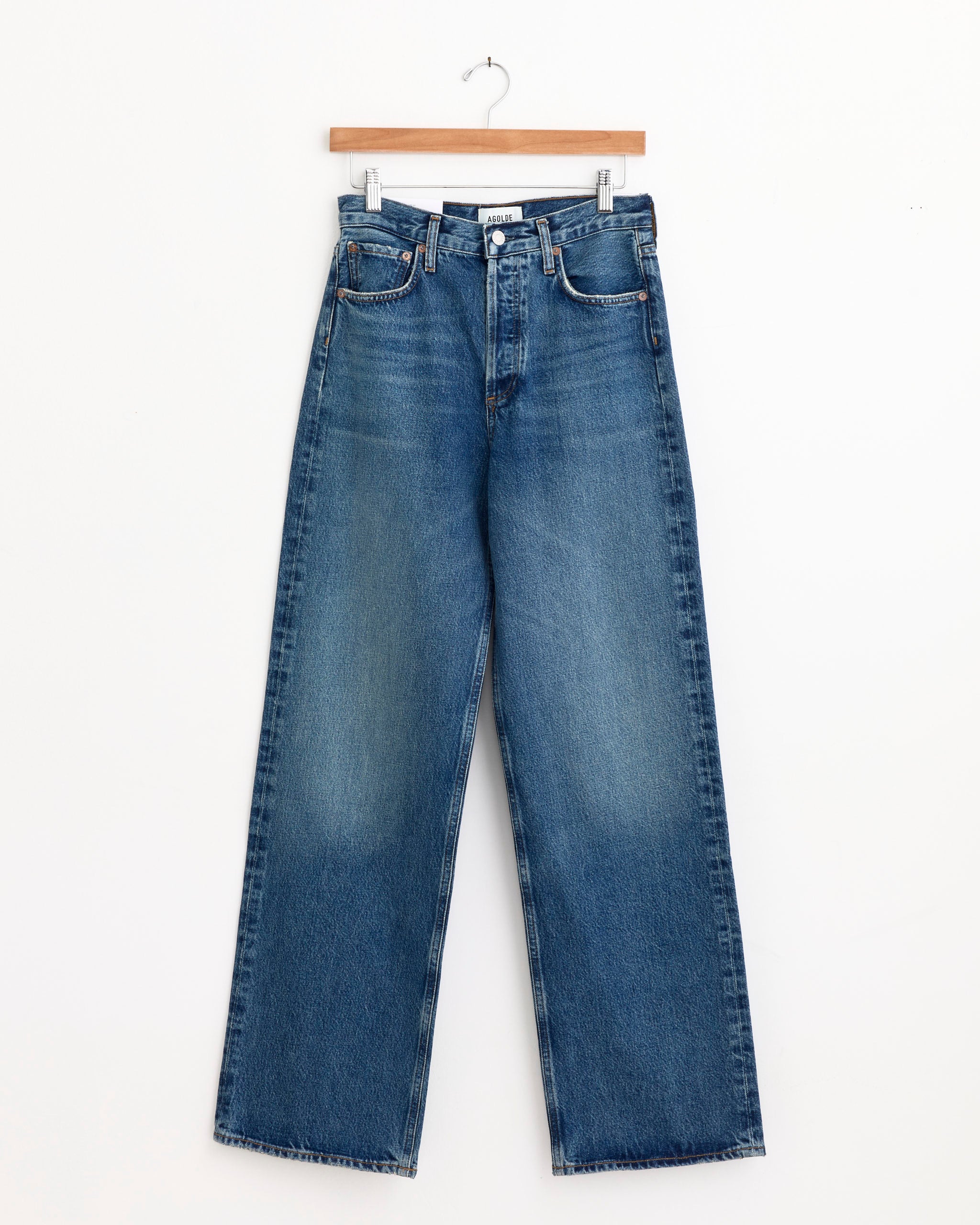 The AGOLDE Ren Jean 32" in Chapter features a high waist, wide-leg fit, and classic five-pocket design in blue denim. Displayed on a wooden hanger against a white background. For sizing help, chat with us online.