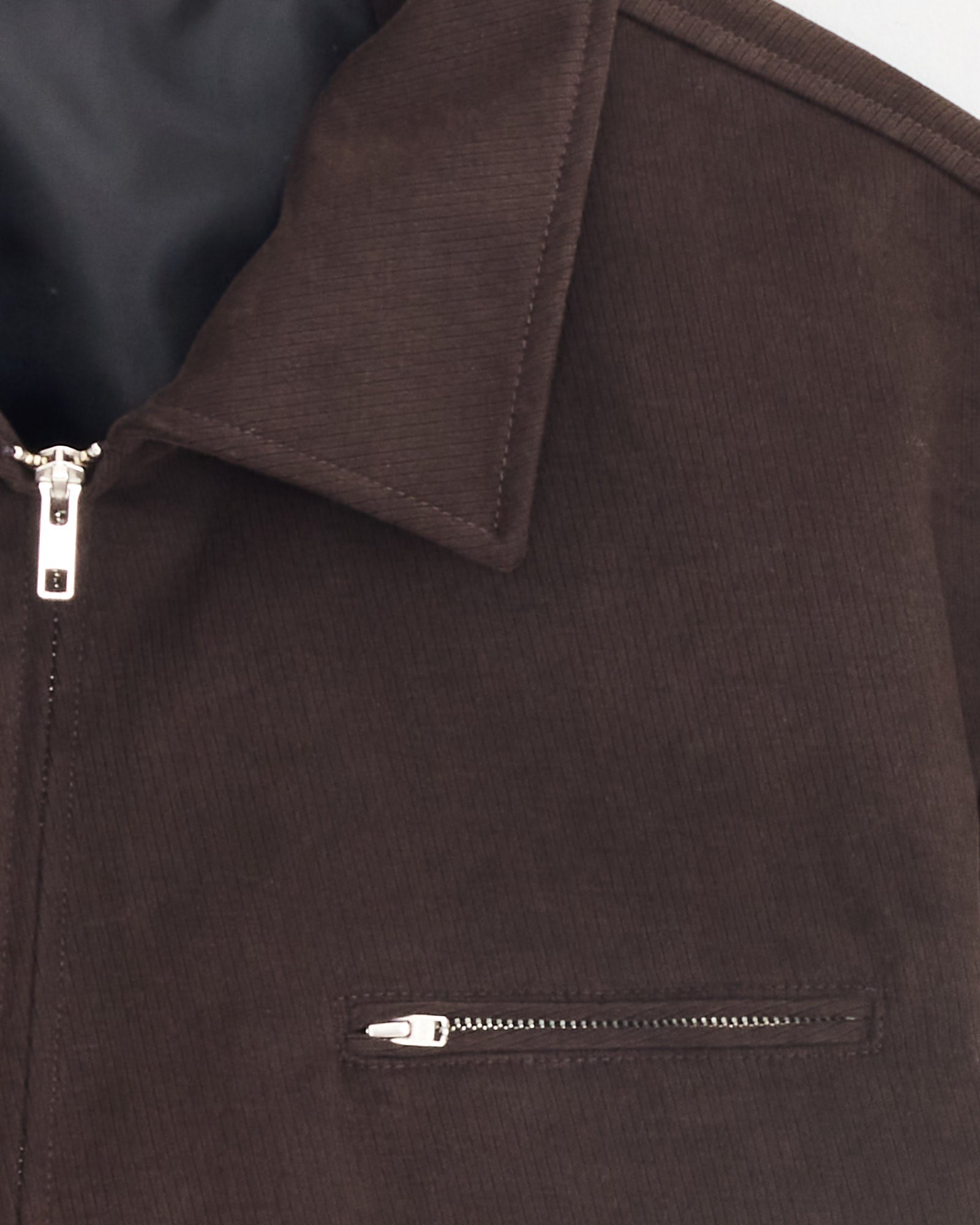 Close-up of the mfpen Postal Jacket in brown, featuring a silver zipper, partial collar, chest pocket with horizontal zipper, and black inner lining.