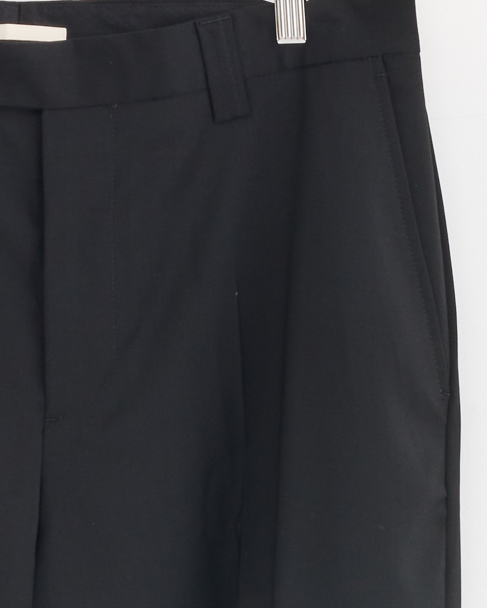 Close-up of the mfpen Study Trouser in Black hanging, highlighting the waistband, belt loop, and side pocket. Crafted from fine Italian wool fabric, shown against a white background.
