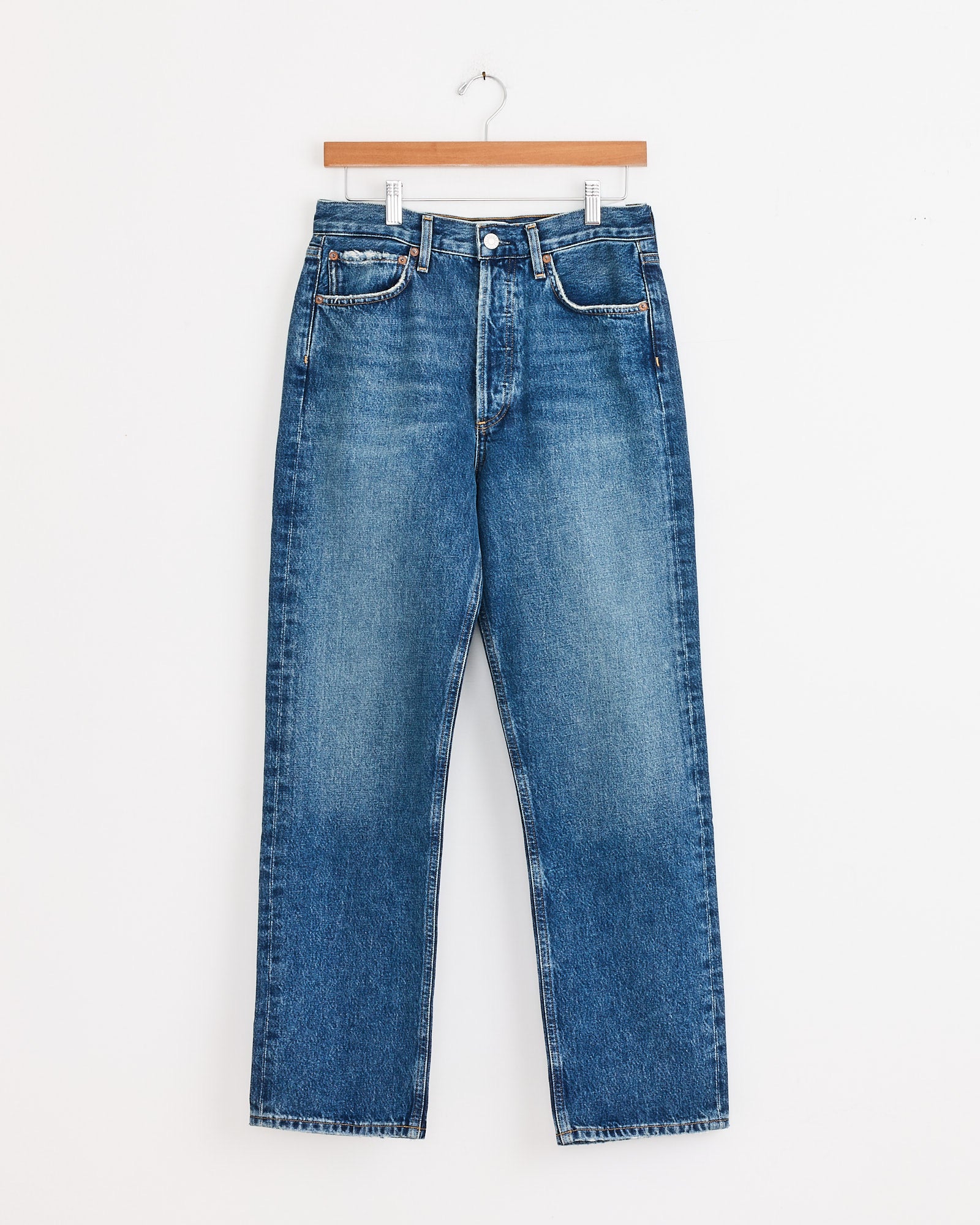 The 90s Jean in Bounty by AGOLDE features a relaxed fit, straight leg, subtle fading, and classic five-pocket styling in regenerative cotton denim. Shown on a wooden hanger against a white background.
