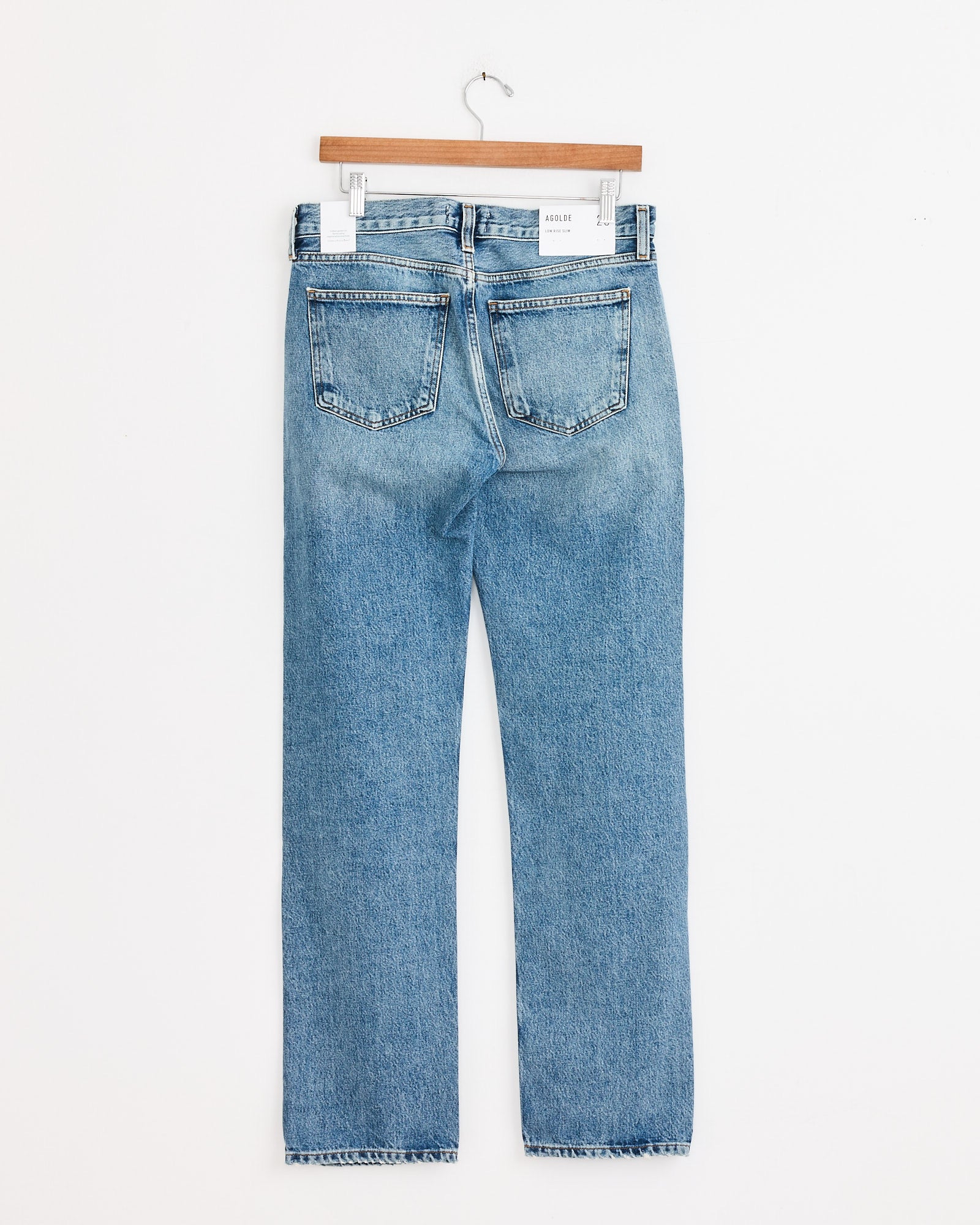 The AGOLDE Low Rise Slim in Downtown jeans, shown with the back facing forward on a wooden hanger against a white background—ideal for viewing fit and details before purchase.