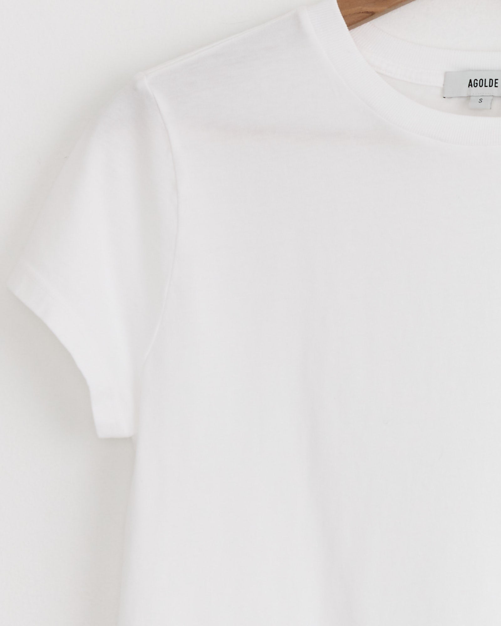 Close-up of the AGOLDE Adine Shrunken Tee in White, displayed on a hanger against a white background, highlighting the upper left section and collar with visible tag—ideal for viewing sizing and fit details.