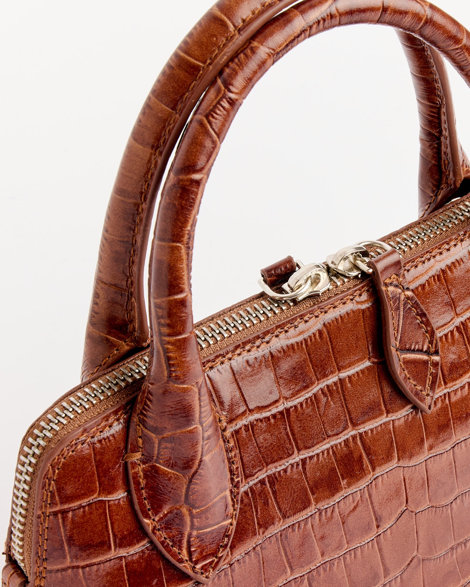 Close-up of the Cordera Mini Crocodile Bag in Caramel, featuring crocodile-embossed leather, double handles, and a silver zipper against a plain white background. For fit help or sizing questions, use our online chat.