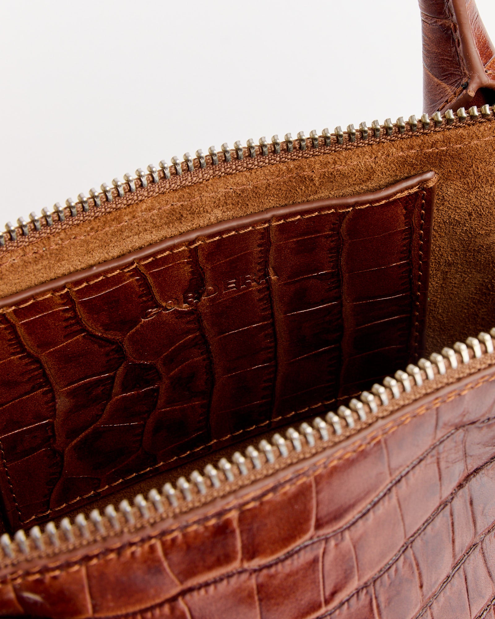 Close-up of the CORDERA Mini Crocodile Bag in Caramel, featuring a brown crocodile finish, suede interior, inner pocket, and a partially unzipped silver zipper.