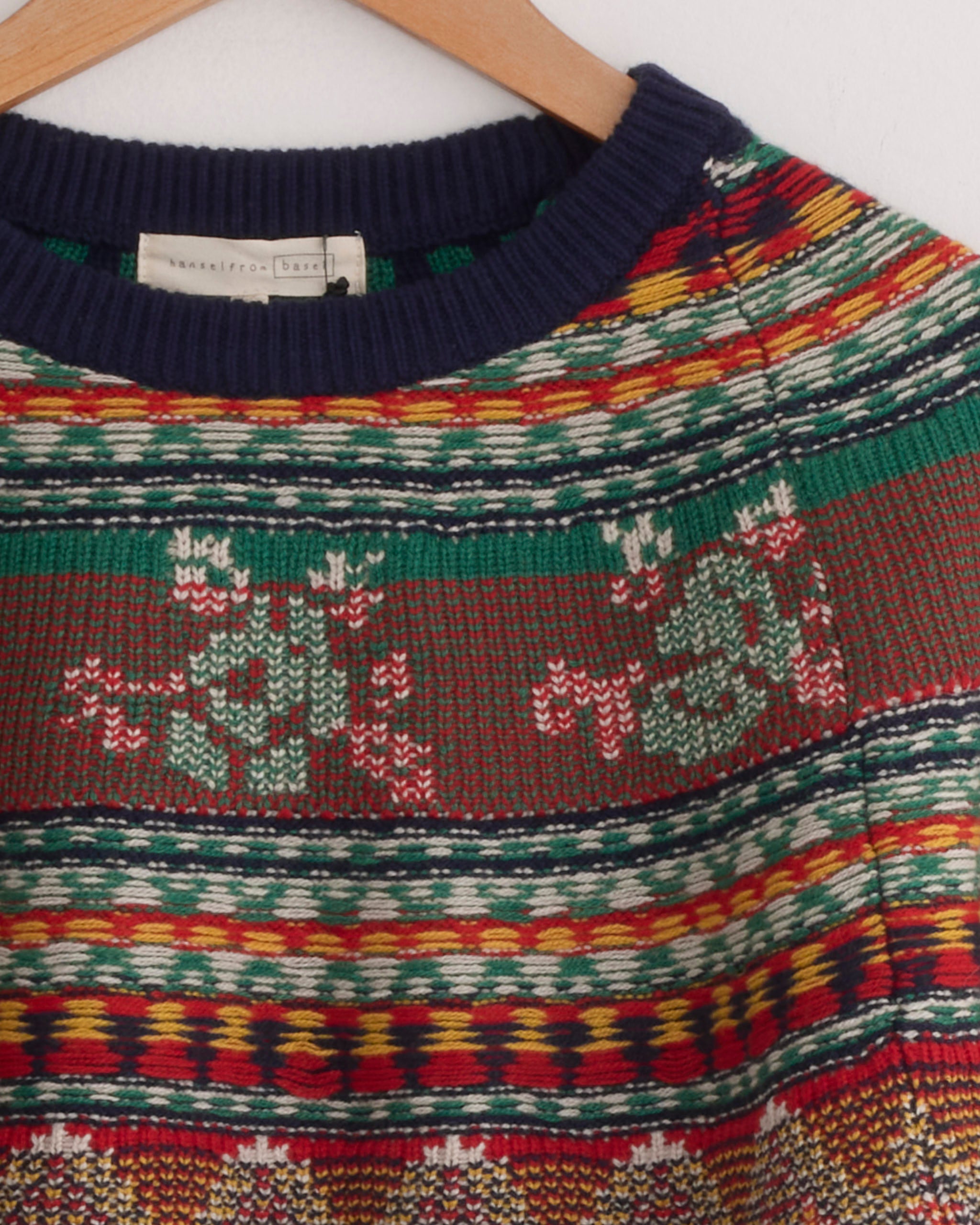 The Mabel Fairisle Pullover in Navy by Hansel From Basel features red, green, yellow, and white stripes with two green reindeer facing each other. Unsure about size or fit? Chat with us online for guidance!.