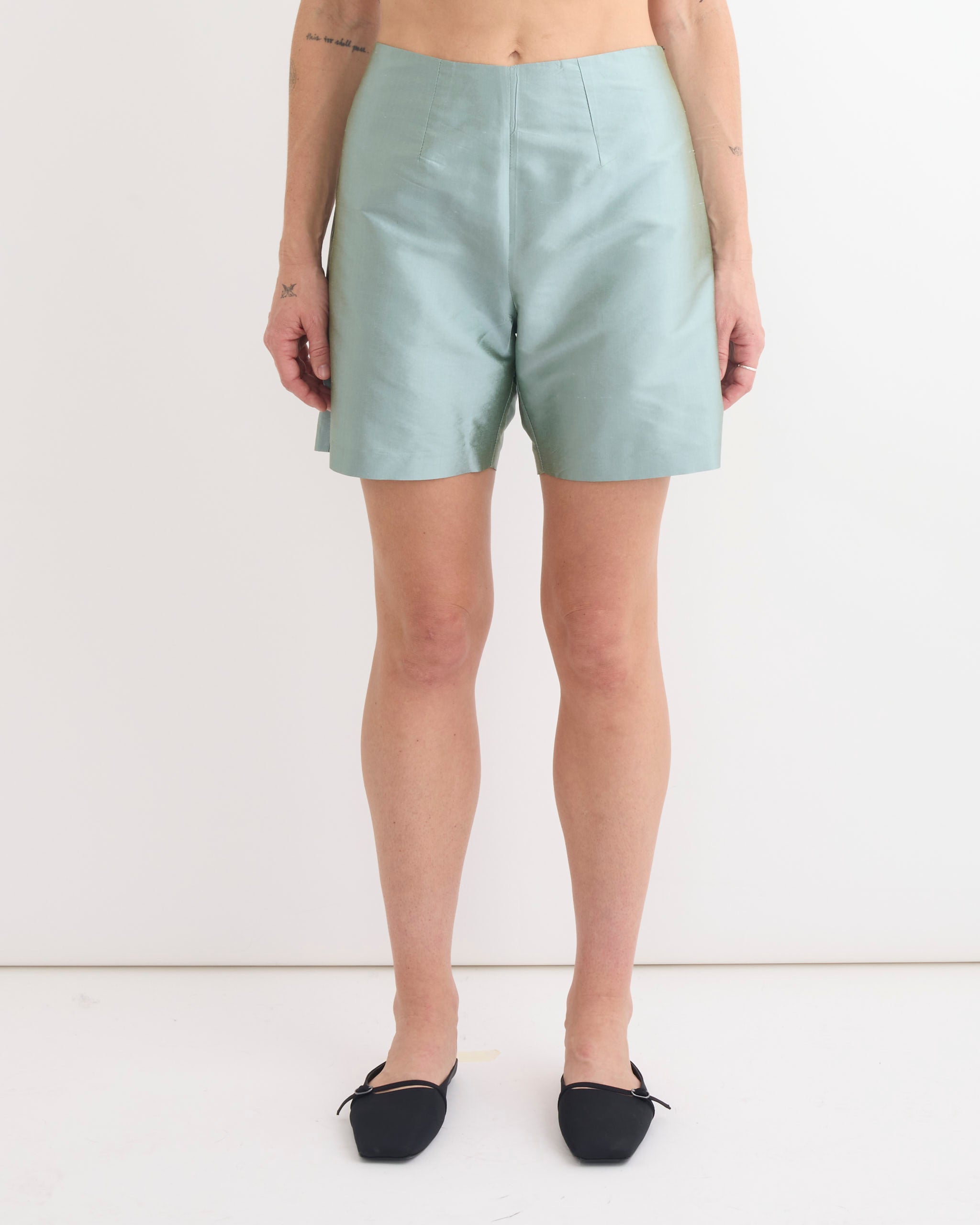 A person wears Chelsea Mak’s Otto Short in Mint Taffeta with black pointed-toe flats, standing against a plain white background with arms relaxed at their sides.