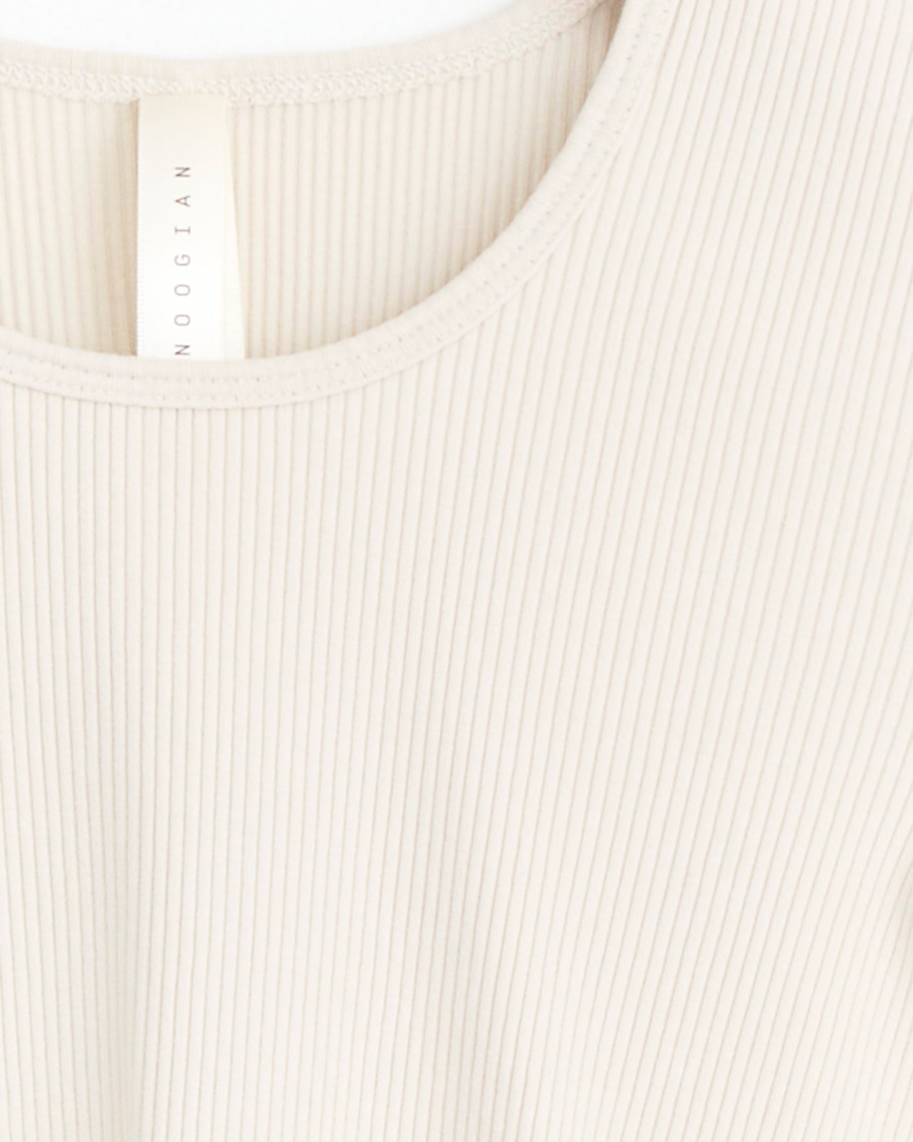 Close-up of the Lauren Manoogian Ruffle Rib Tee in Greige, featuring cream-colored ribbed fabric and a round neckline. A white tag in the collar shows Peru as the country of origin, with texture and ribbing details clearly visible.