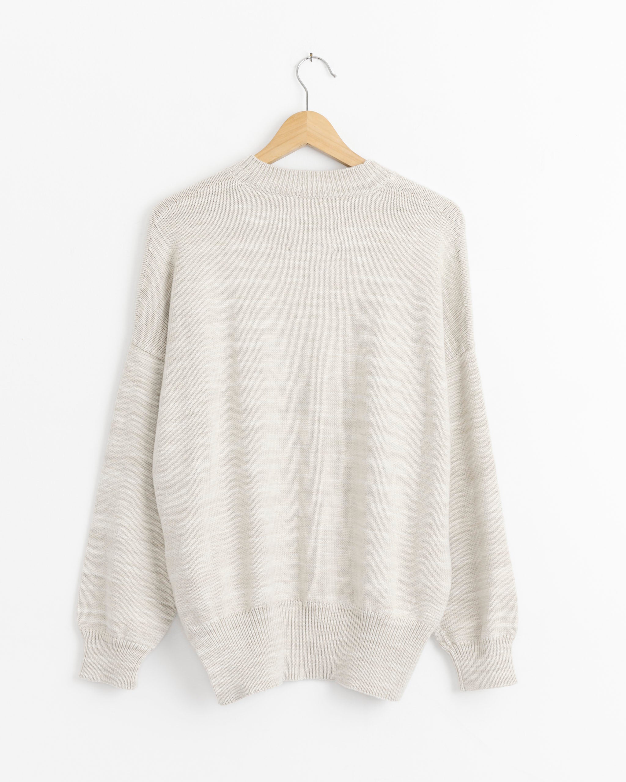 The Lauren Manoogian Watercolor Crewneck in Parchment, a light beige cotton pullover with long sleeves, is displayed from the back on a wooden hanger against a plain white background.