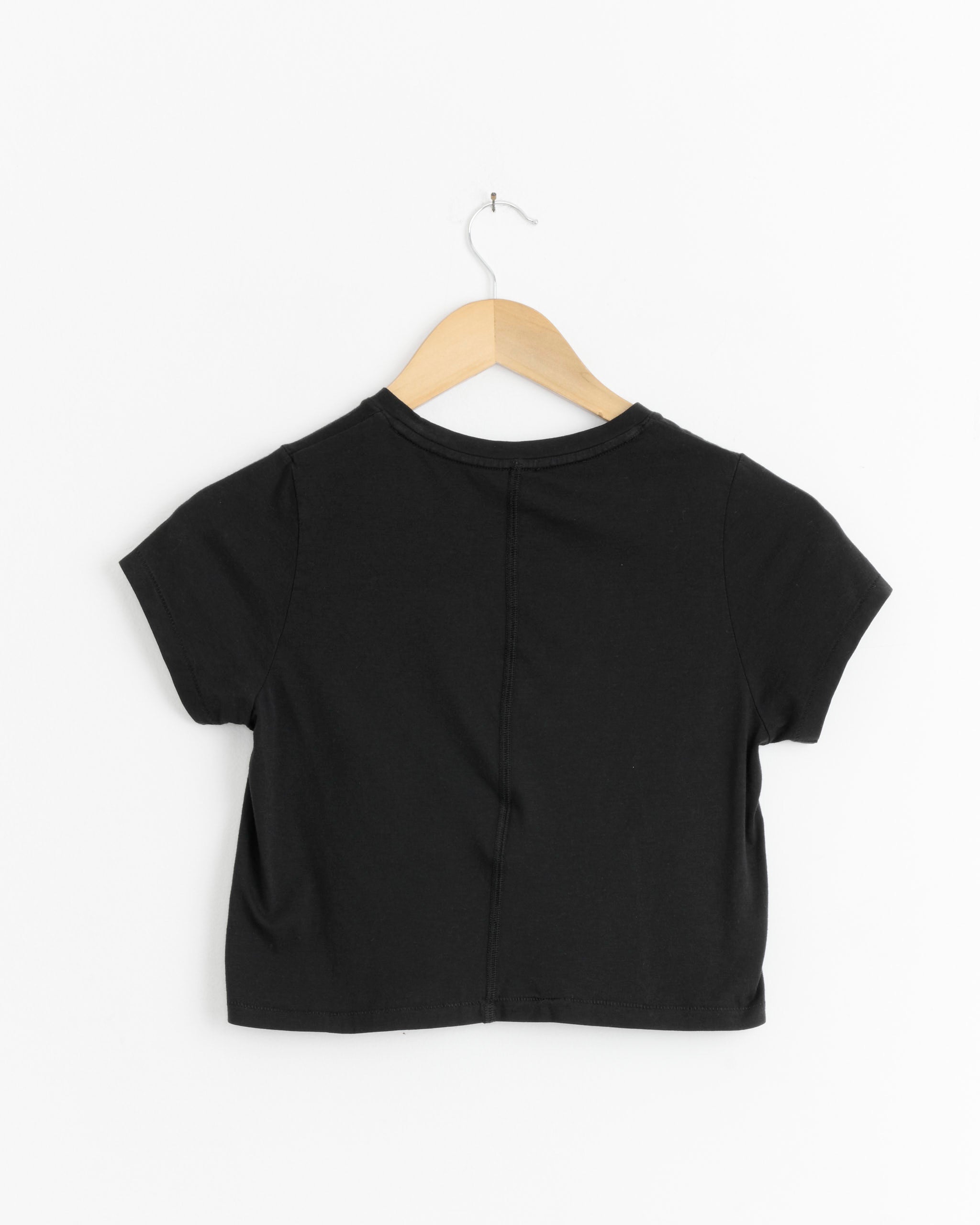 The Lauren Manoogian Fine Crop Tee in Black, crafted from soft Pima cotton, is shown from the back on a wooden hanger against a white background.
