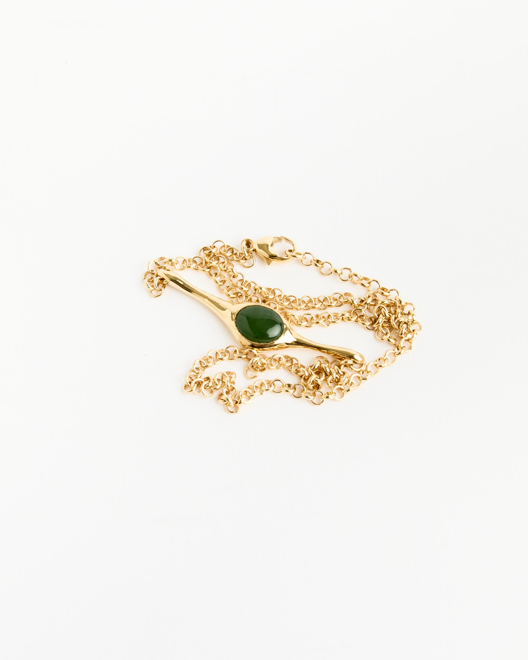 The Faba Necklace by Faris features a gold-plated bronze chain with a green jade pendant, elegantly coiled on a white background—a true example of sculptural jewelry sophistication.