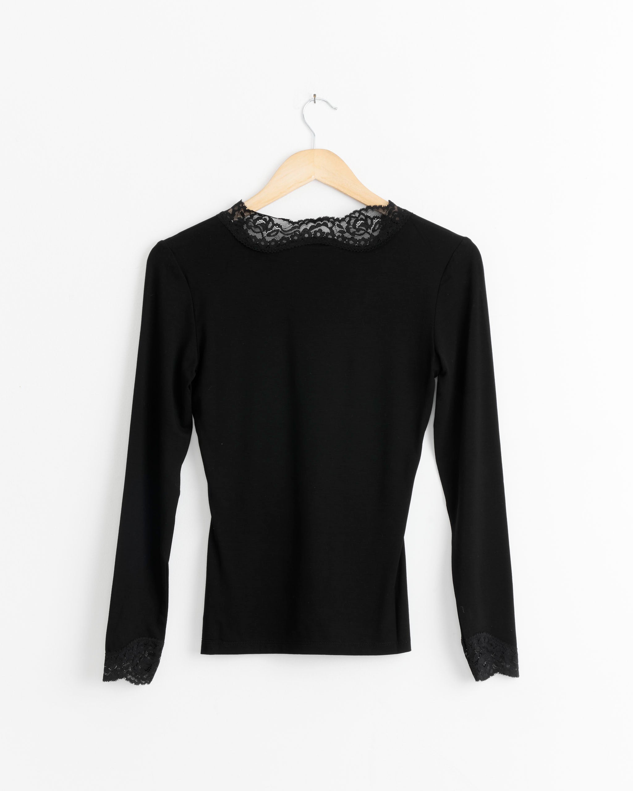 The Bruna Blouse in Black by Beaufille, featuring decorative lace trim on the collar and cuffs, hangs elegantly on a wooden hanger against a white background.
