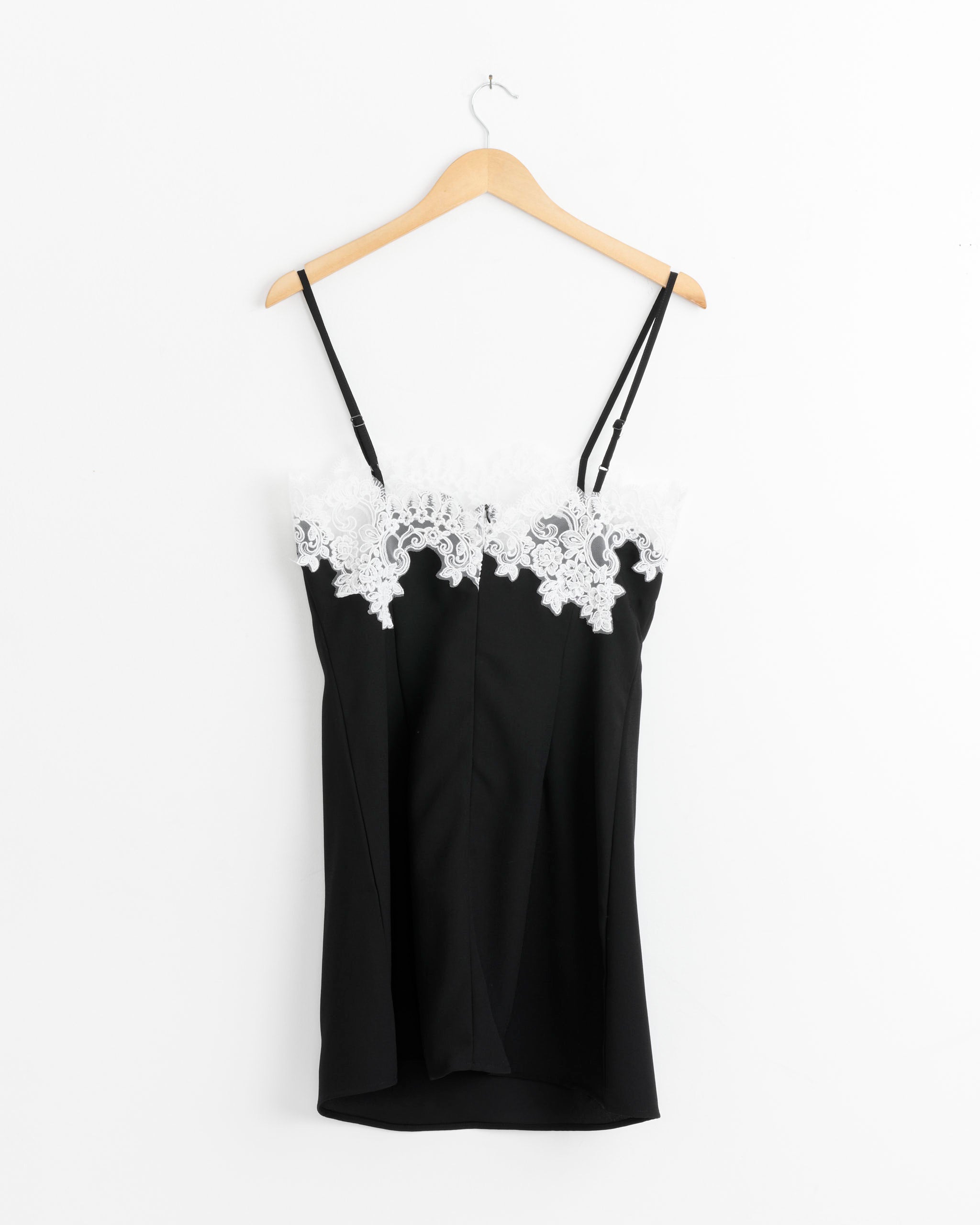 A black sleeveless camisole with thin straps and white lace trim on the neckline hangs on a wooden hanger, ideal for layering under the Beaufille Medina Dress in Black or styling with your favorite mini slip dress.