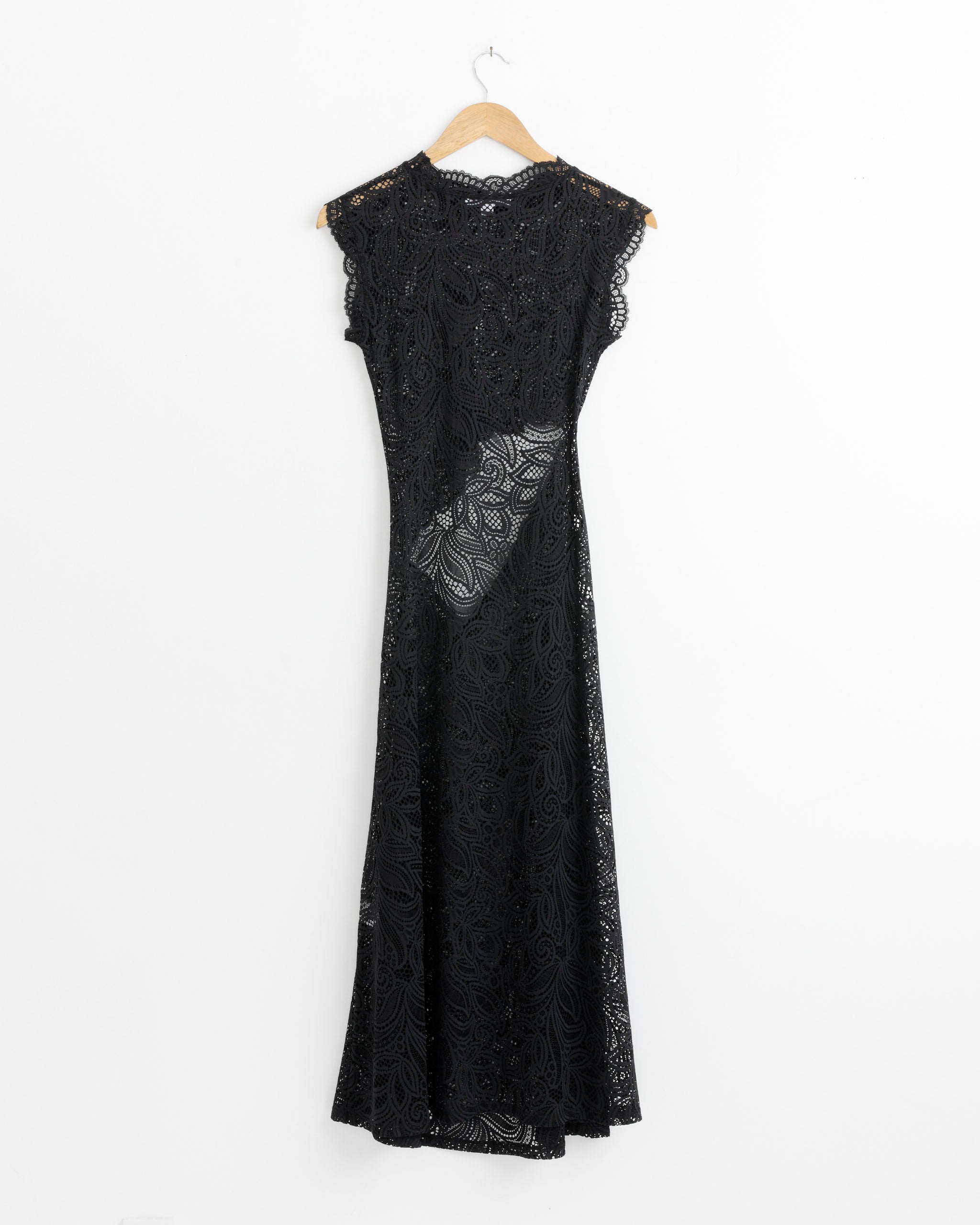 The Beaufille Silva Dress in Black is a sleeveless midi dress featuring long black lace, a high neck, and scalloped edges. It hangs on a wooden hanger against a plain white background.