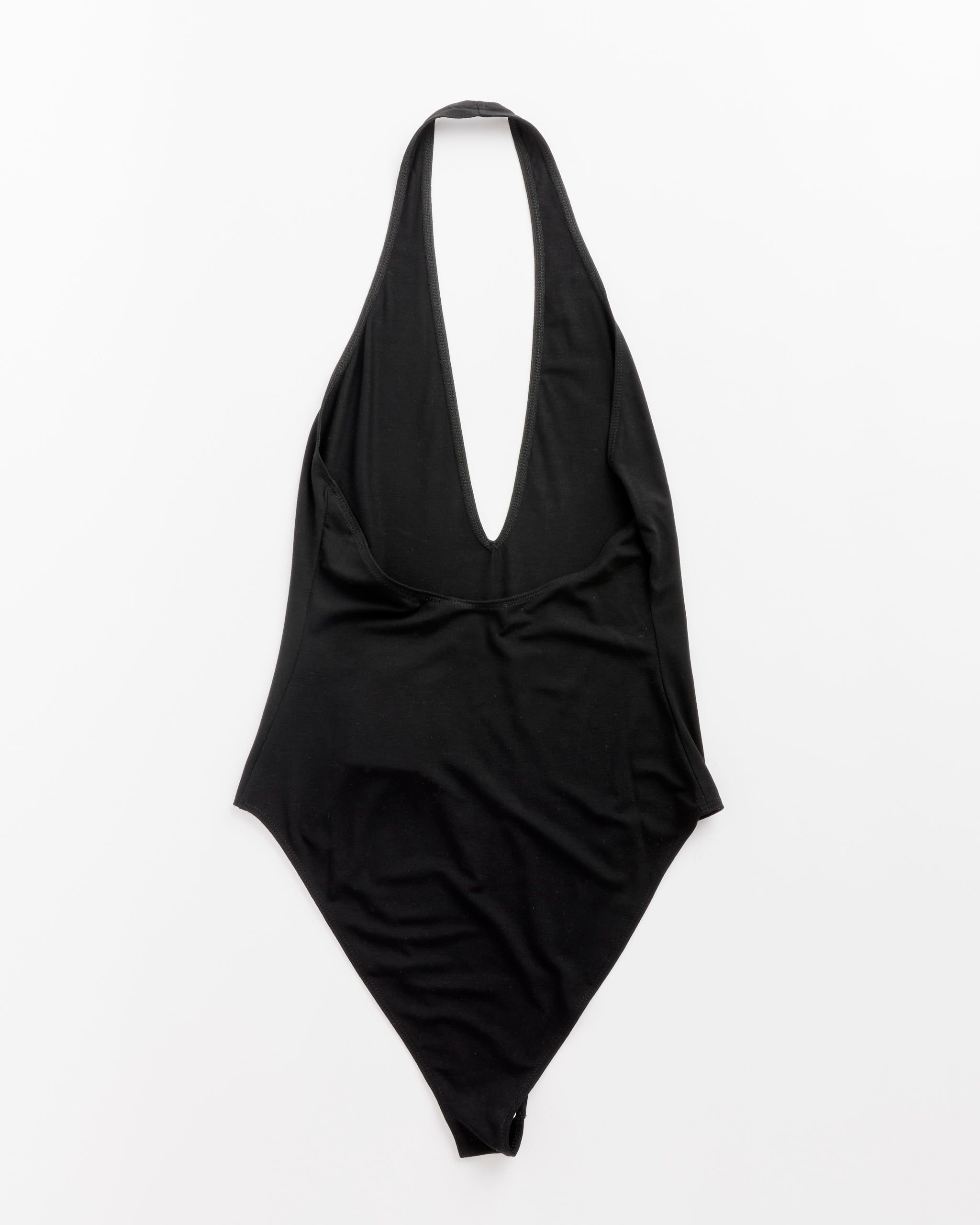 The Franz Bodysuit in Black by Beaufille, a one-piece swimsuit with a deep V neckline and halter design, is laid flat on a white background.