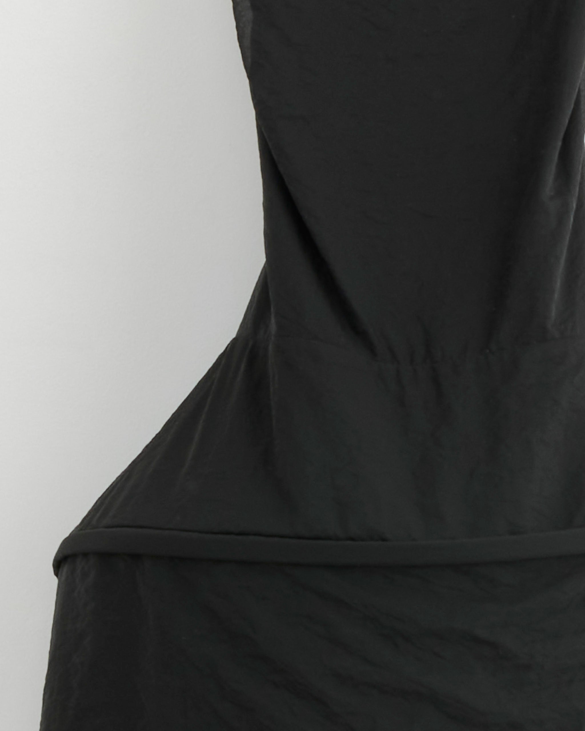 Close-up of Tibi’s Chassis Hoop Strappy Dress in Black, showcasing its sculptural silhouette, angular waist details, and textured fabric. Set against a plain light background to highlight this modern black dress.