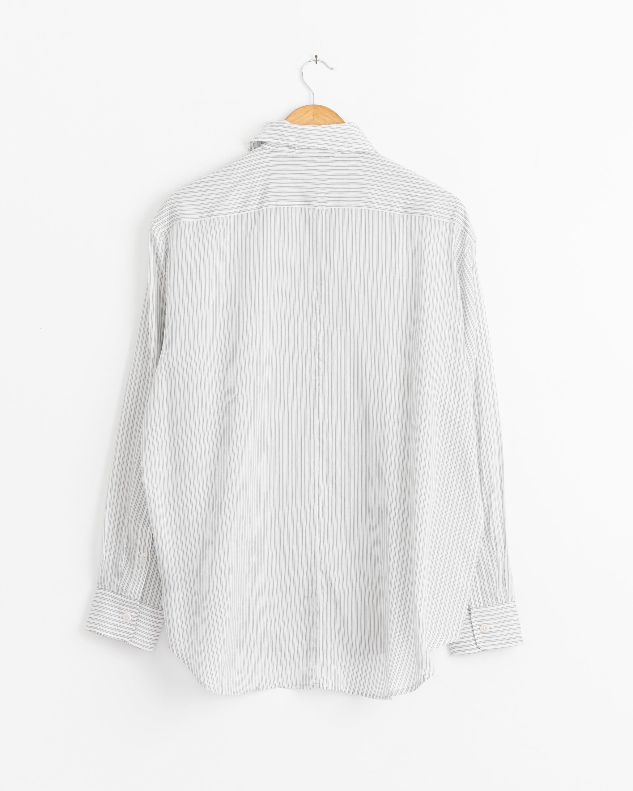 The Tibi Ultra Light Silk Tercel Stripe Pintucked Shirt in White Grey Multi hangs on a wooden hanger, displayed from the back against a plain white wall.