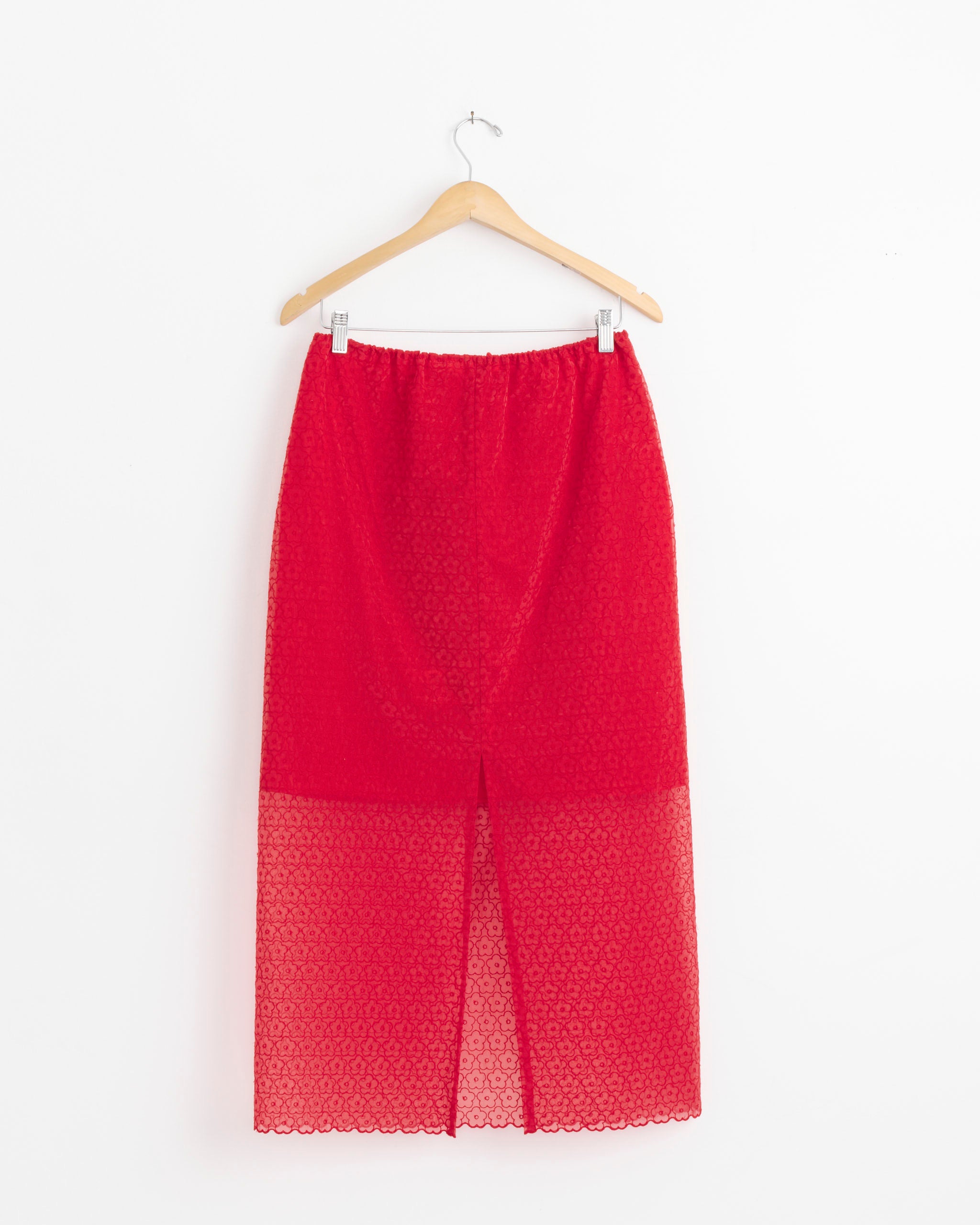 The Cecilie Bahnsen Donna Skirt in Red Windflower Embroidery features a knee-length sheer overlay with a front slit, shown on a wooden hanger against a plain white background.