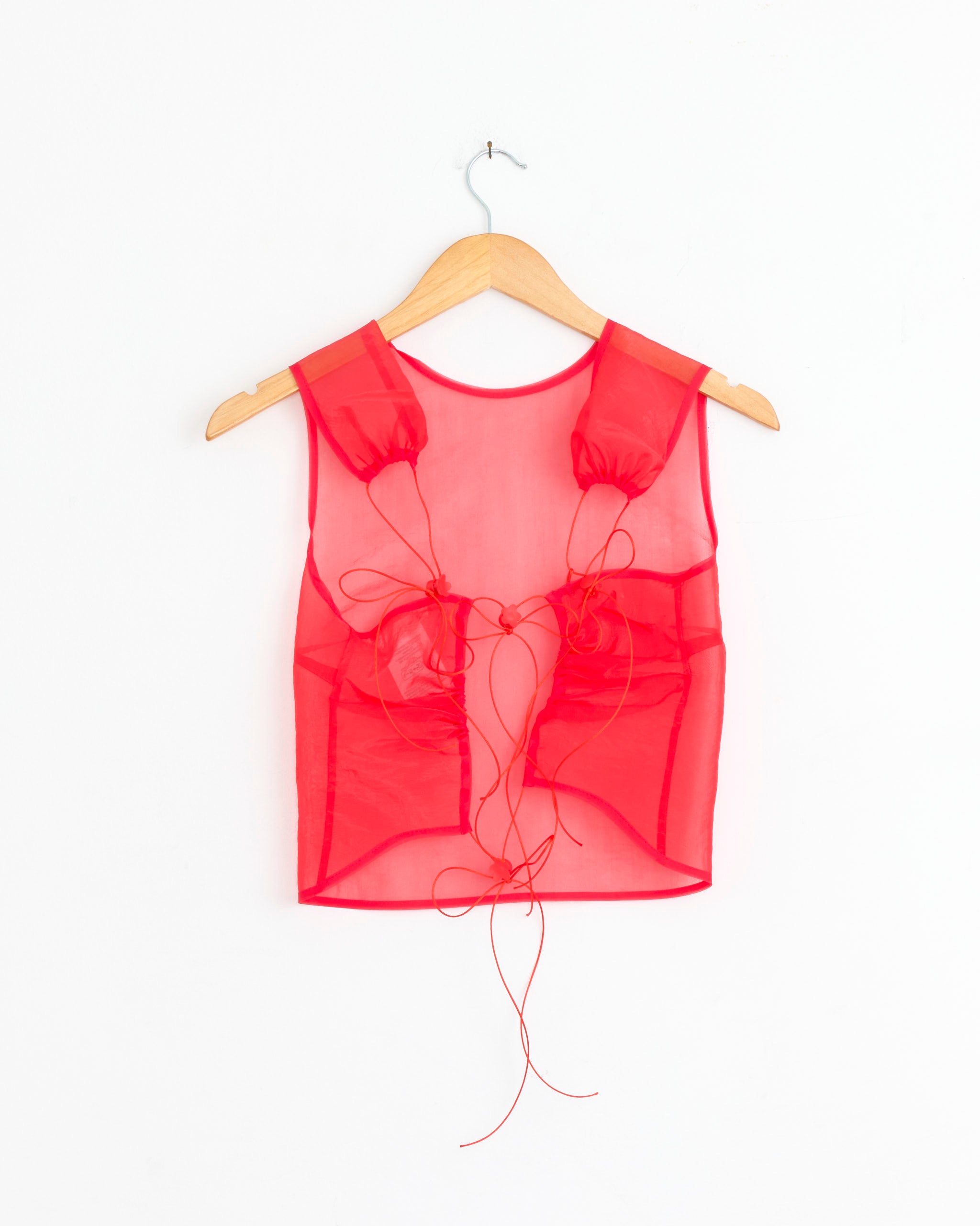 The Katia Top in Red Liquid Myrtia by Cecilie Bahnsen is a sheer organza sleeveless crop top with ruched details and red string ties, shown on a wooden hanger against a white background. Crafted from polyamide polyester.