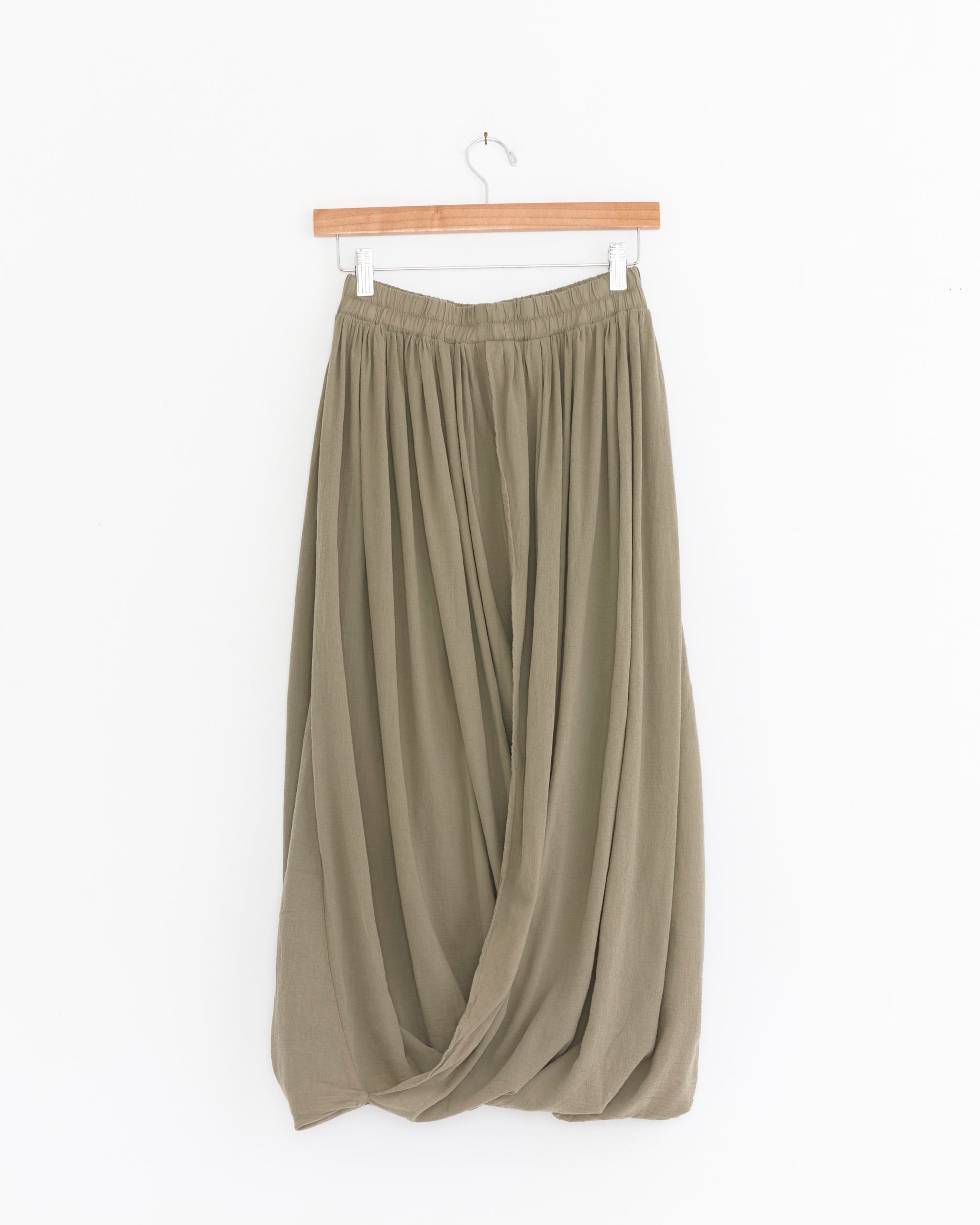 The Black Crane Greek Column Skirt in Cement is a long skirt made in the USA, with a gathered elastic waistband and draped, overlapping textured cotton gauze panels, shown hanging on a wooden hanger against a white background.