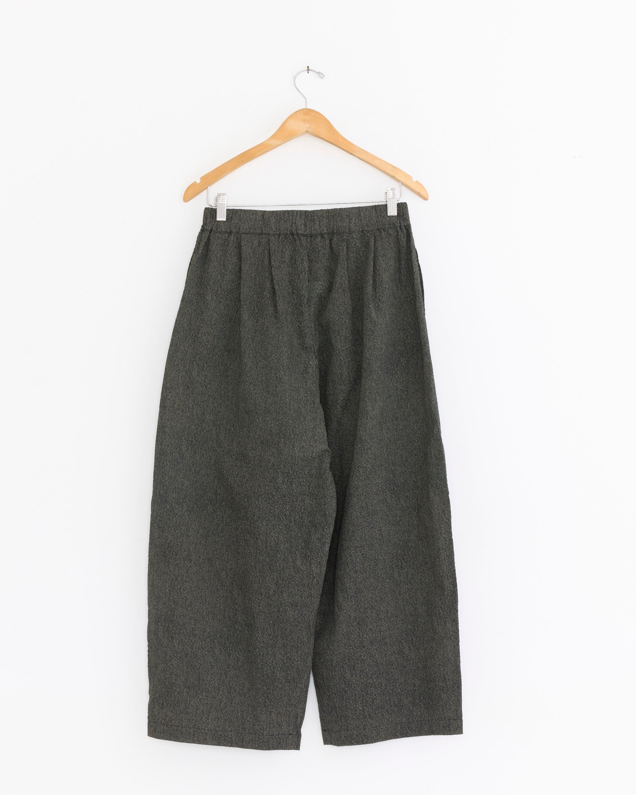 The Wide Pant in Steel by Black Crane, made from Japanese cotton with a high waist and elastic waistband in dark gray, is displayed on a wooden hanger against a plain white background.