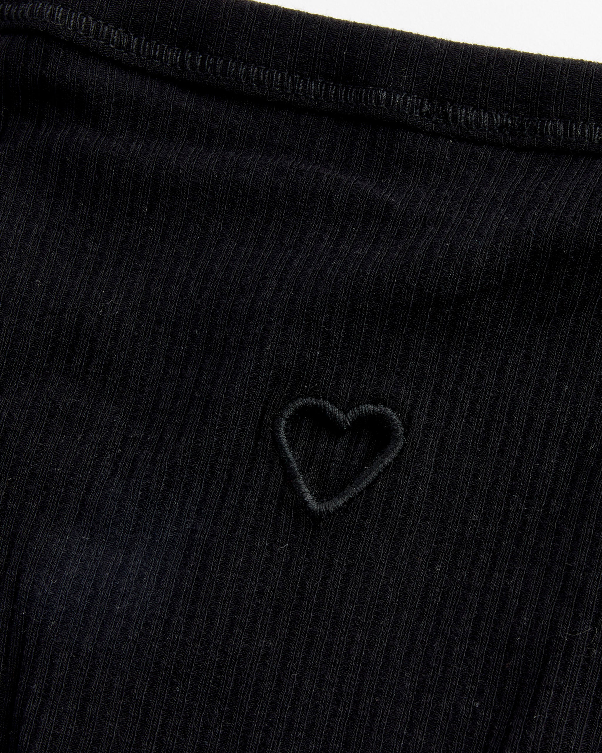Close-up of the Baserange Heart Bell Pants in Black, featuring subtly ribbed fabric and a small stitched heart outline at the center. A seam runs near the top edge, highlighting its unique detailing.
