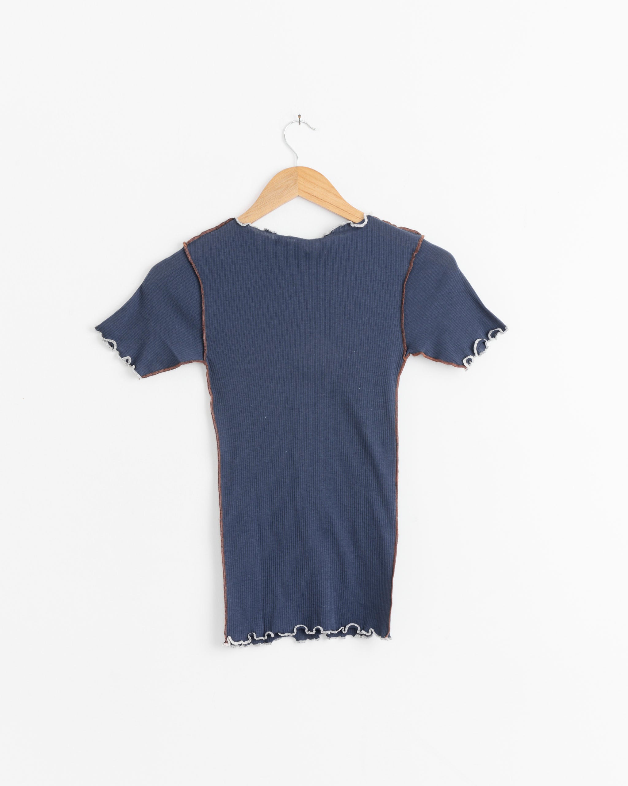 The Baserange Vein Tee in Preston Blue, a short-sleeve organic cotton rib boatneck with contrast stitching and frilled edges, hangs on a wooden hanger against a white background.