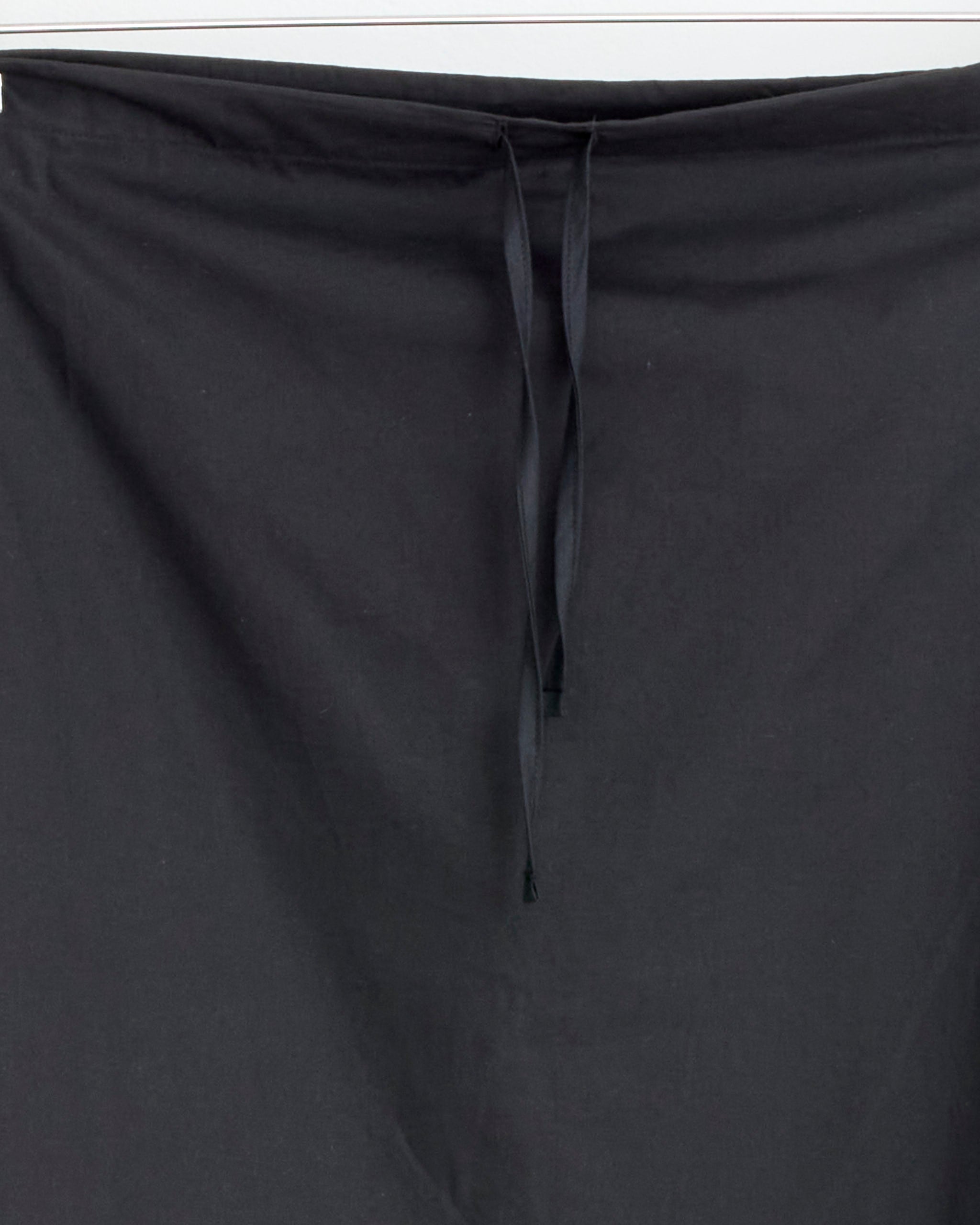A close-up of the Baserange Pictorial Skirt in Black, made from organic cotton, features two black drawstrings down the center that highlight its adjustable design against a plain background.