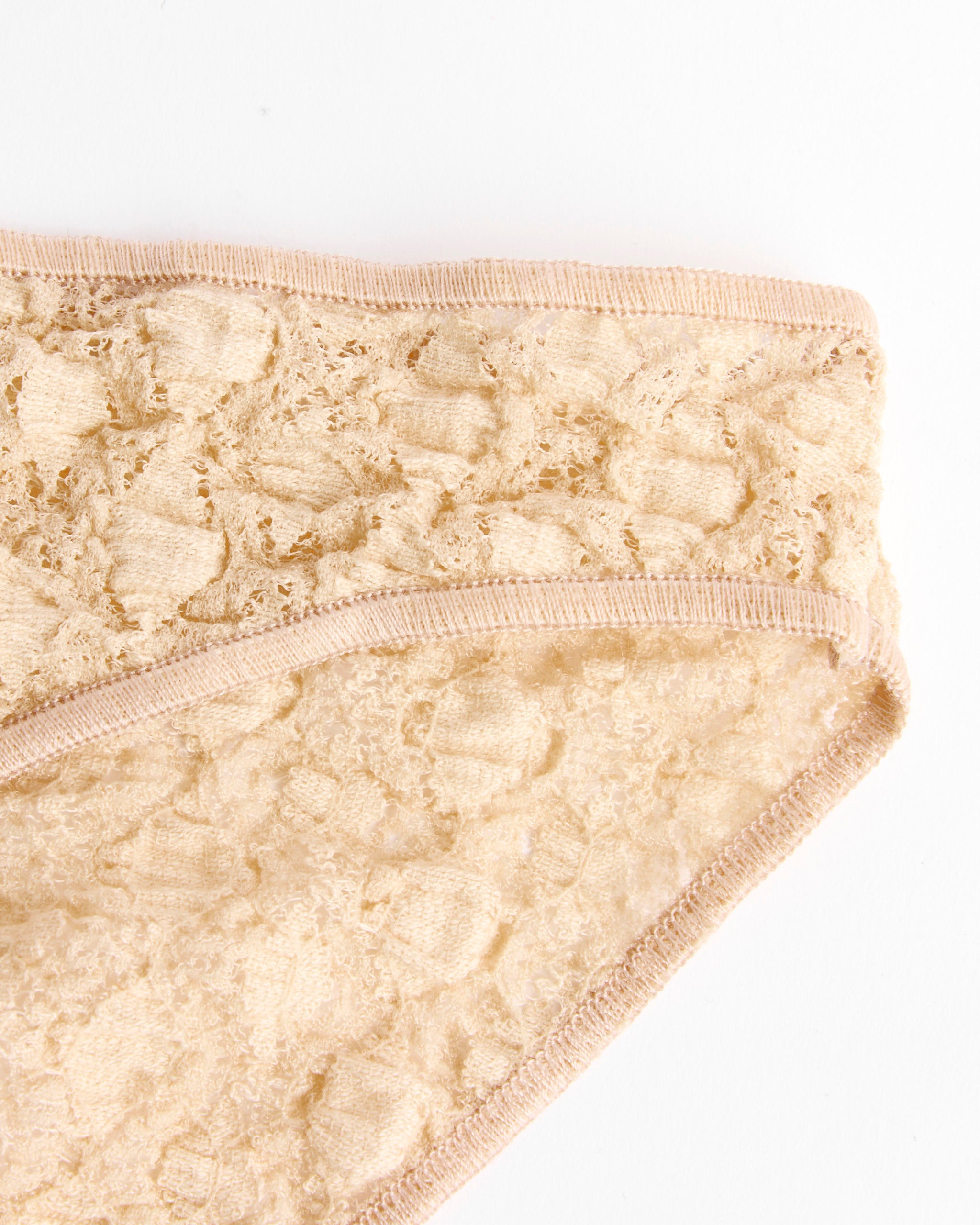 Close-up of the corner of Baserange Crescent Pants in Dylan Beige, highlighting the delicate floral lace and smooth fabric edging. Set against a white background, these bikini briefs are inspired by timeless organic cotton underwear style.