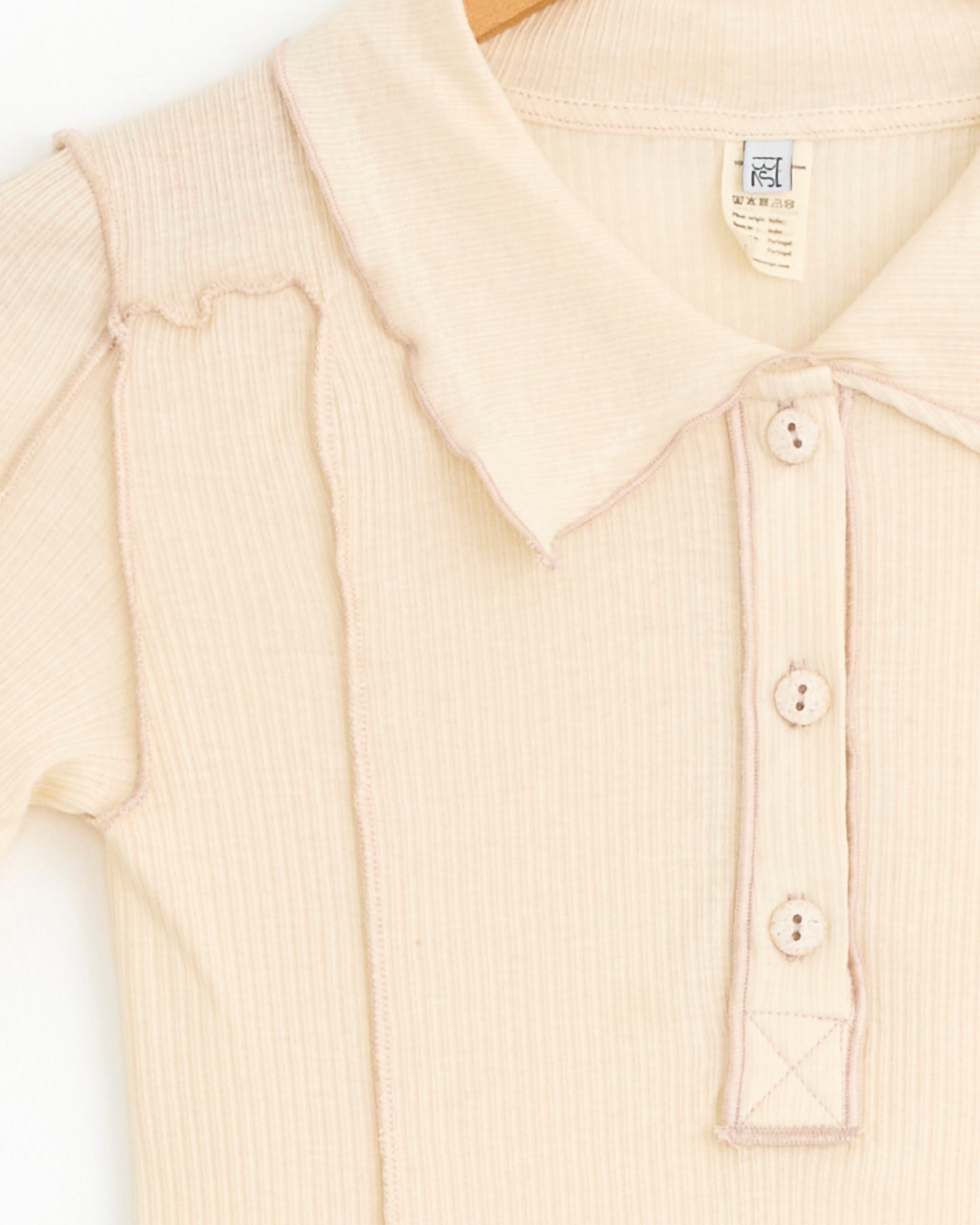 Close-up of the Omato Polo Tee Shirt in Off White by Baserange, featuring ribbed organic cotton, short sleeves, a pointed collar with three buttons, and decorative exposed pink stitching.