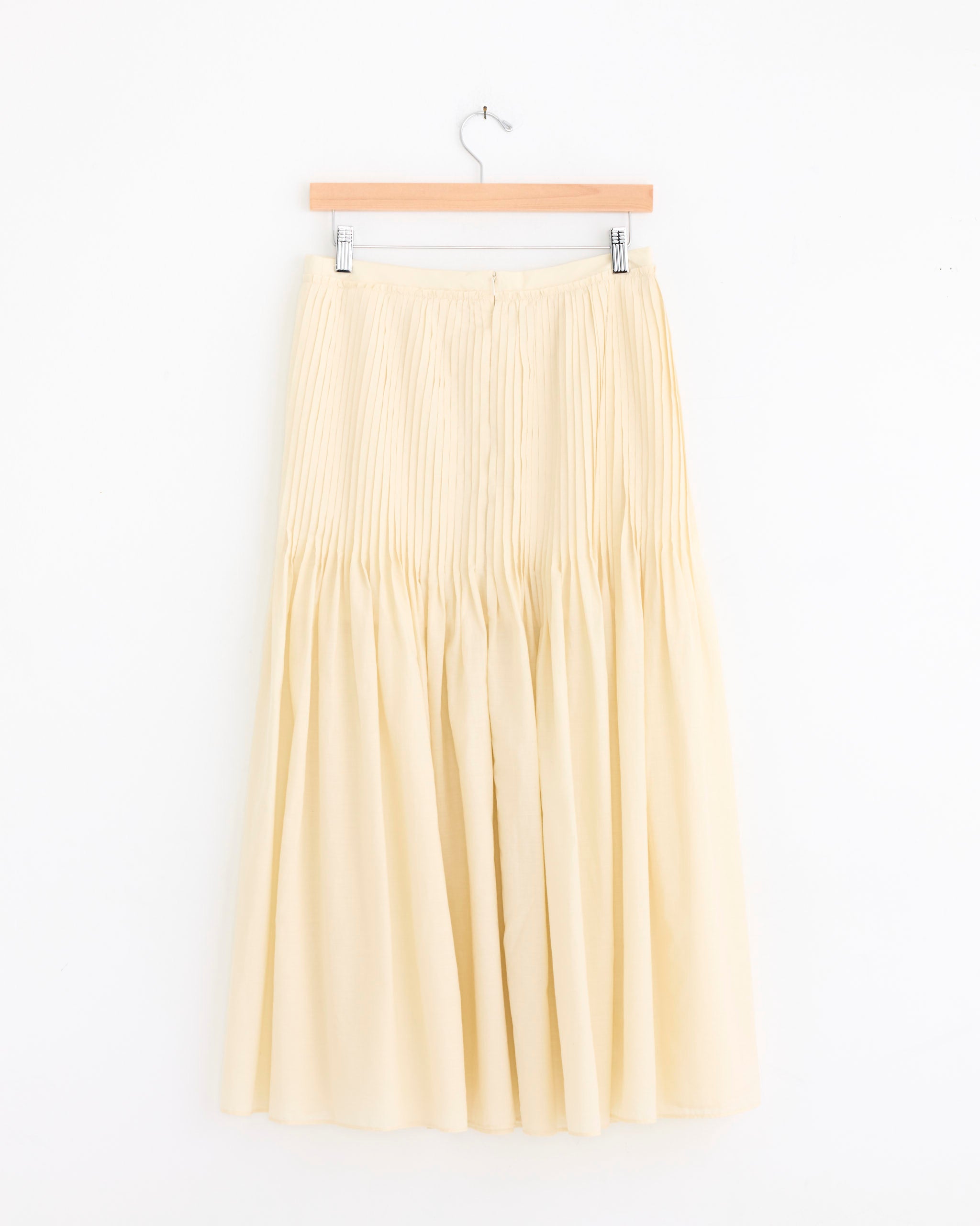 The Auralee Super Fine Cotton Lawn Pin Tuck Skirt in Ivory White hangs on a wooden hanger against a plain white background.