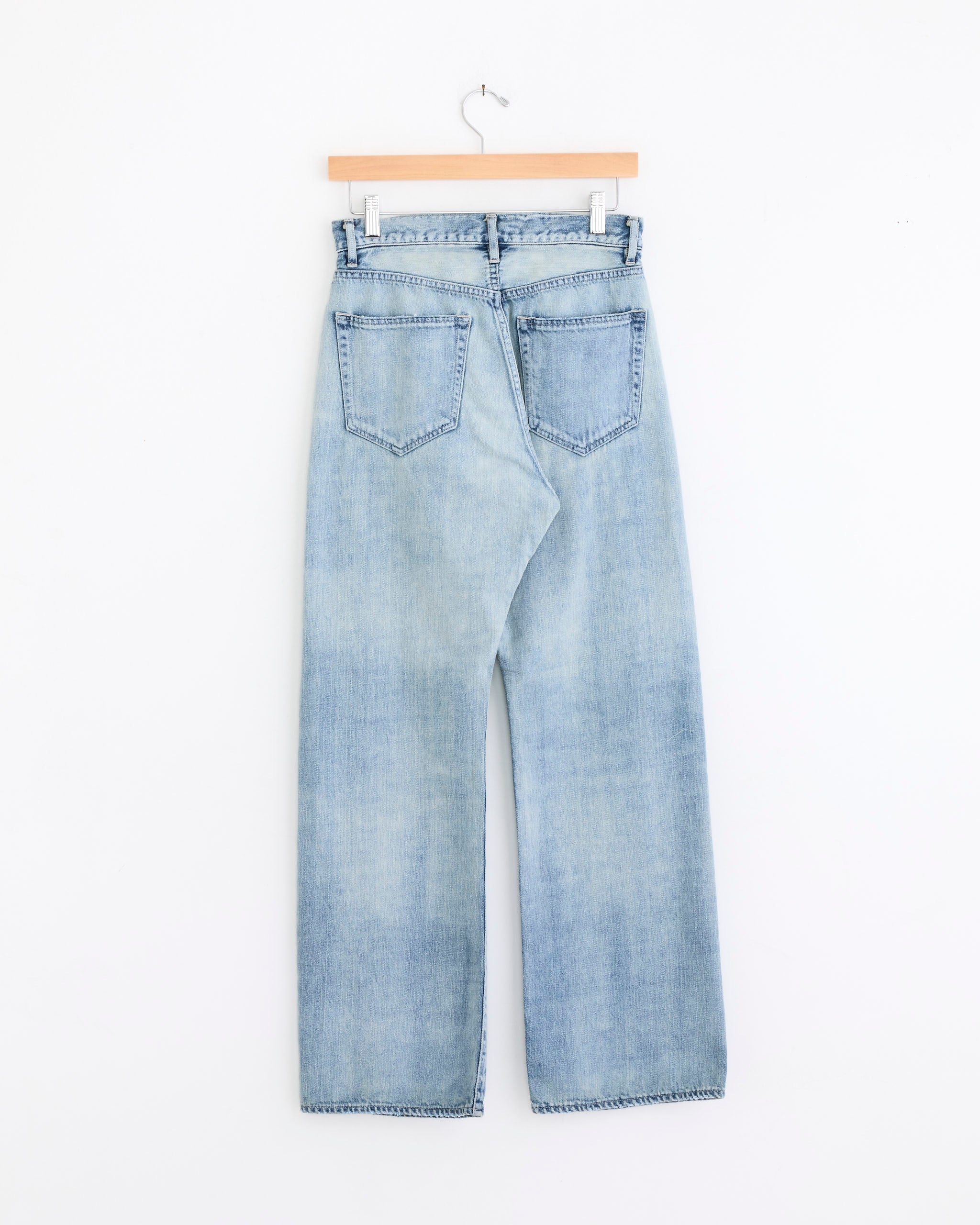 Auralee’s Faded Selvedge Light Denim Pant in Light Indigo is a high-waisted, straight-leg jean with rear pockets and belt loops, crafted from premium Japanese selvedge denim and shown on a hanger against a white background.