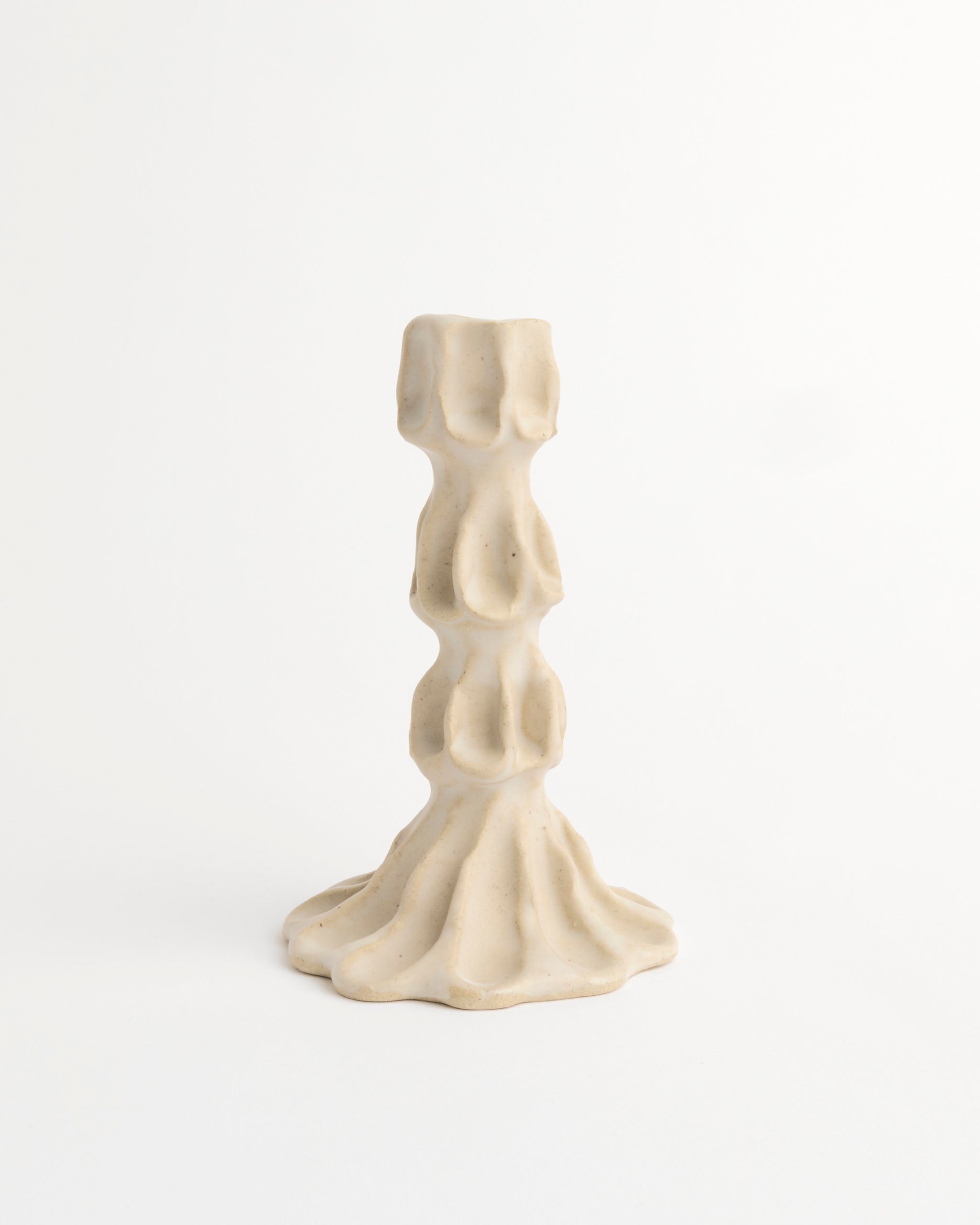 The Large Candle Stick by Carma Ferrier Ceramics is a beige sculpted ceramic holder with an irregular, melted-wax-inspired design, standing out elegantly against a white background.