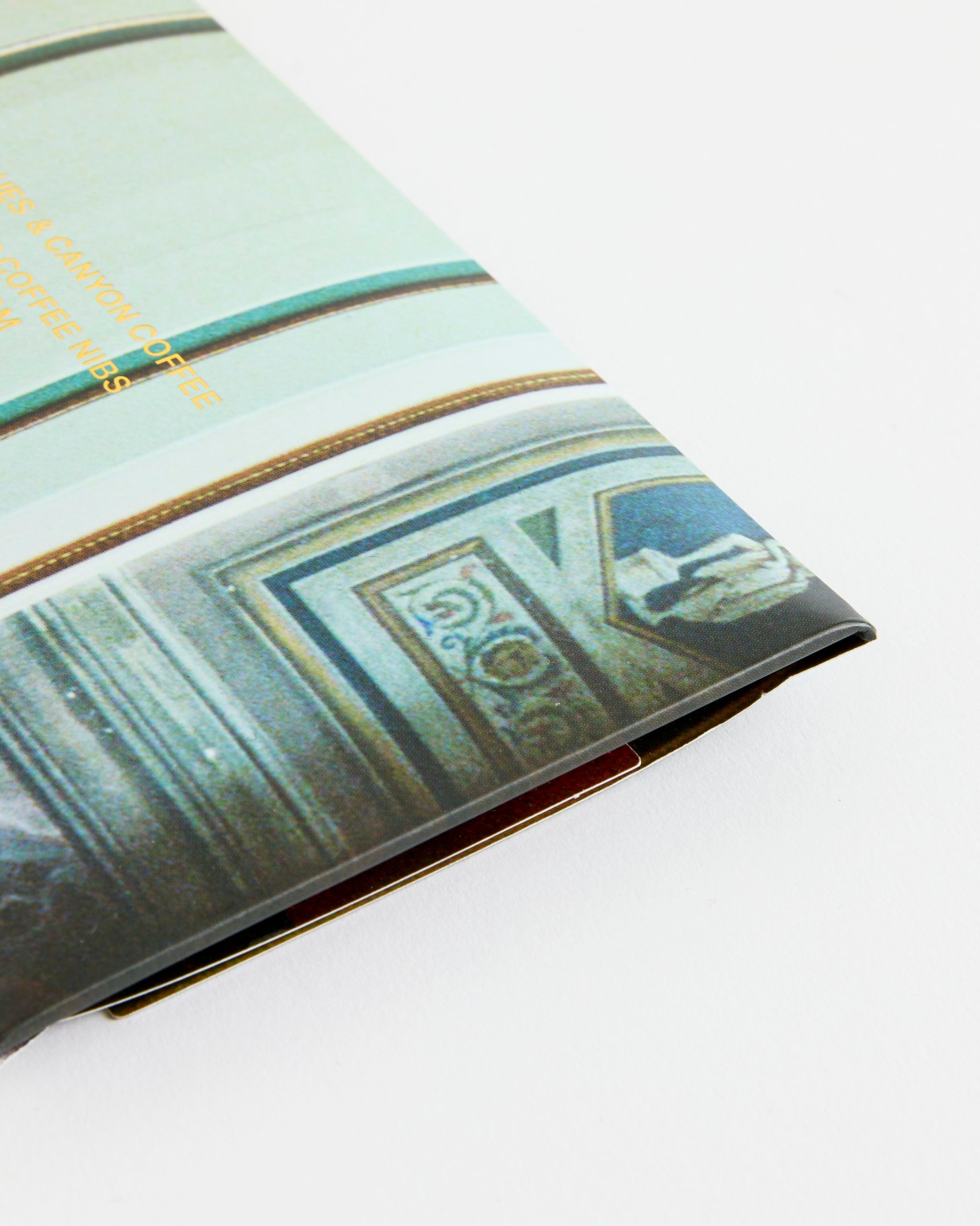 A close-up of a folded piece of printed paper with architectural details and gold text on a white surface, partially revealing Casa Bosques Canyon Coffee Chocolate.