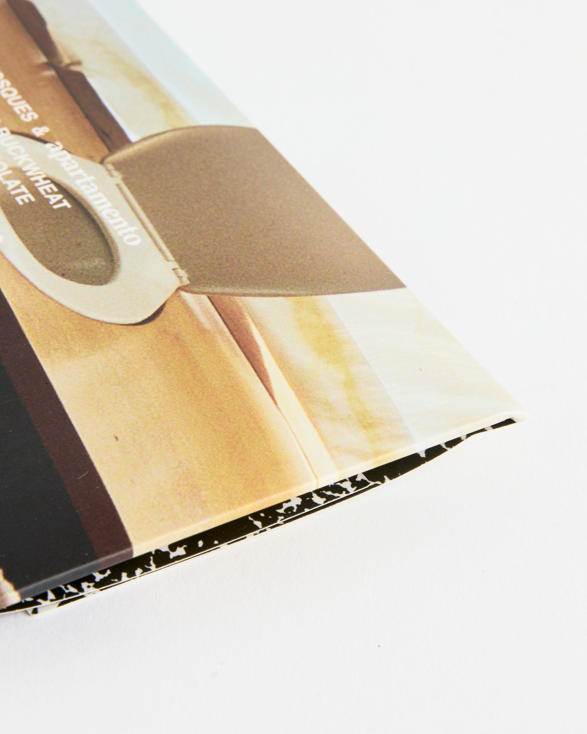 A close-up of a worn, slightly bent Toasted Buckwheat x Apartamento Chocolate cover by Casa Bosques, showing minor fraying at the edge against a white background.