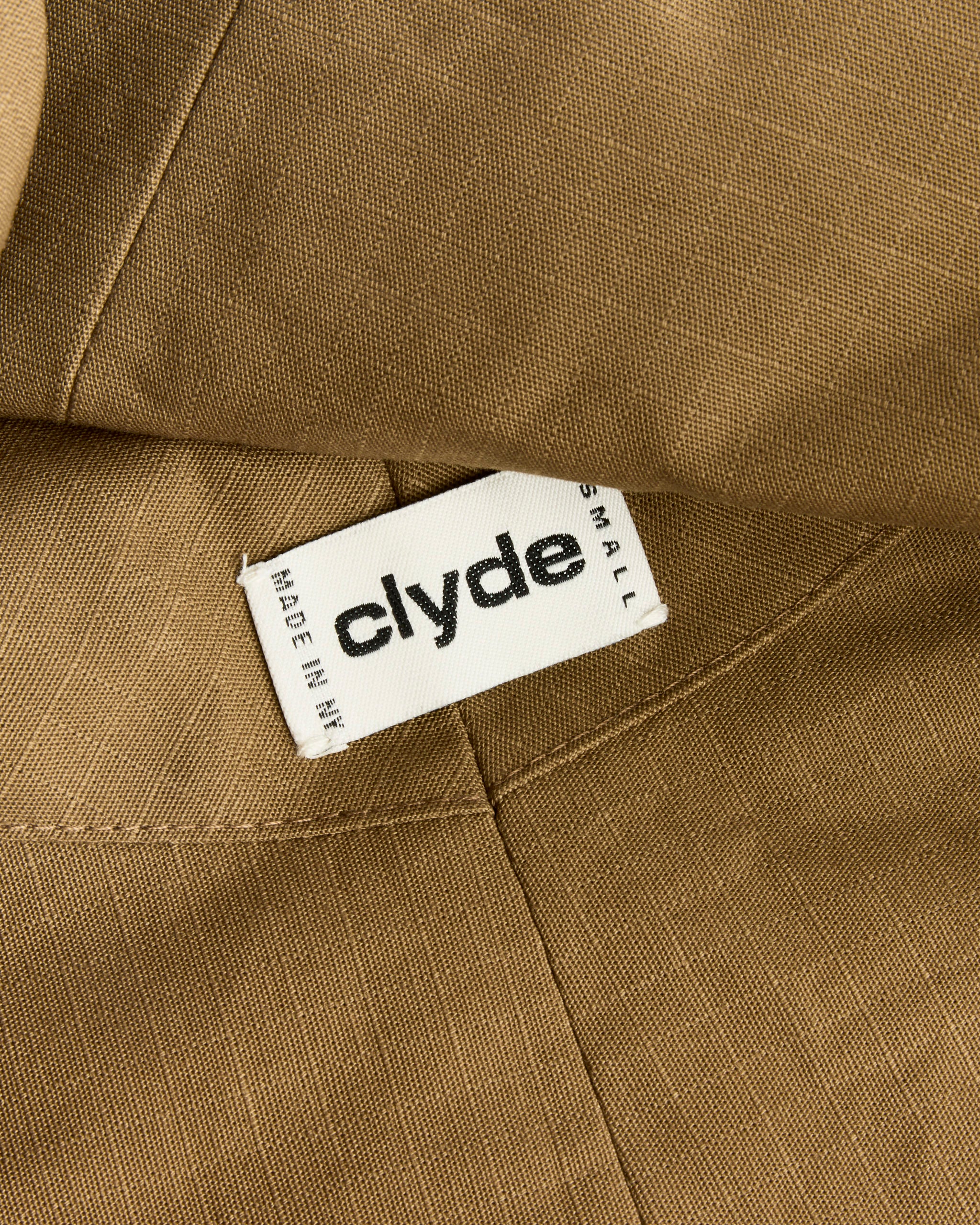 A close-up of the Iona Hat in Caramel Rip Stop by Clyde shows a white label reading "clyde," "MADE IN NEW YORK," and size "SMALL"—an authentic detail from this collection.