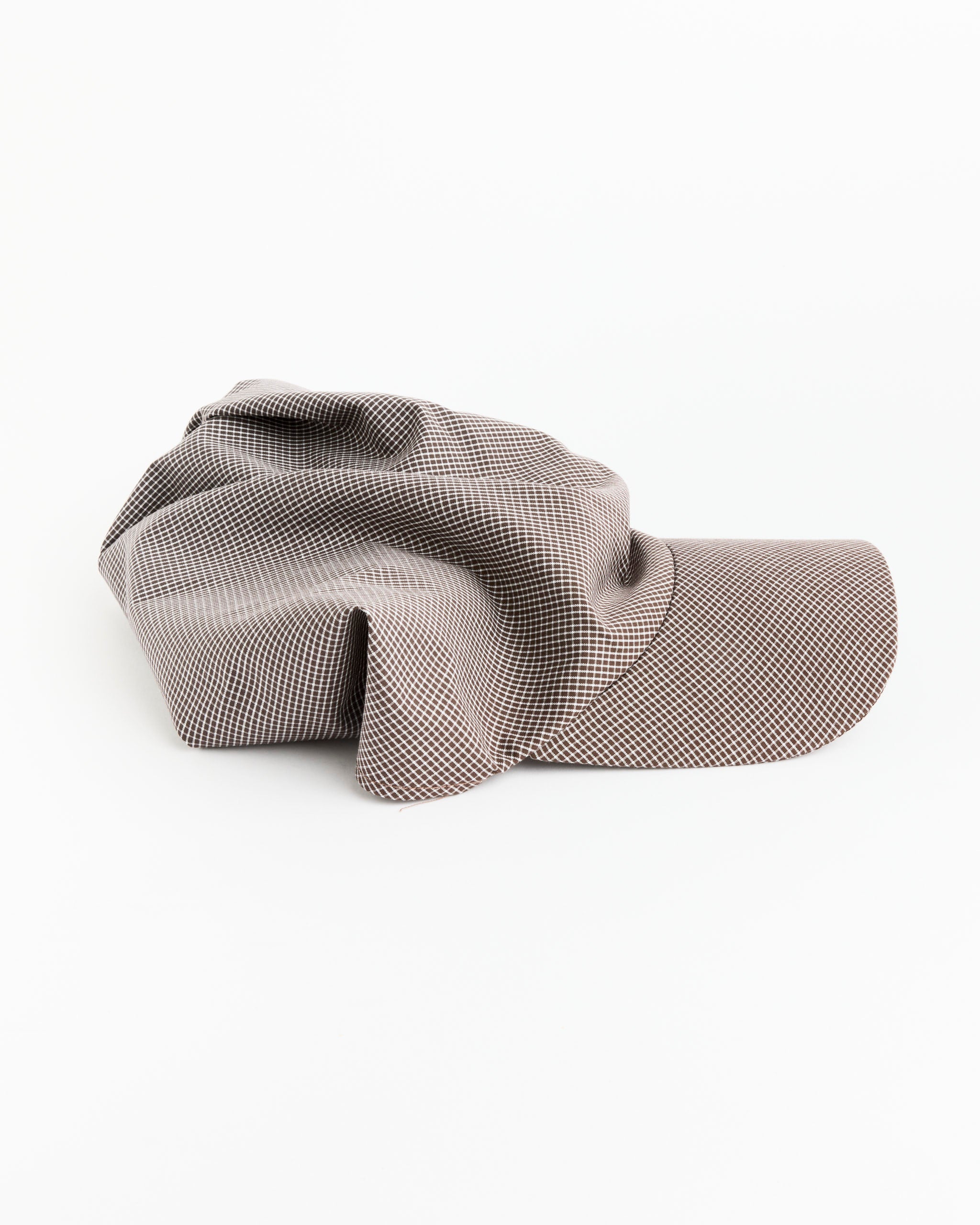 The Brimmed Scarf in Chocolate Gingham Poplin by Clyde is displayed on a white surface, with its crown slouched and the brim facing right.