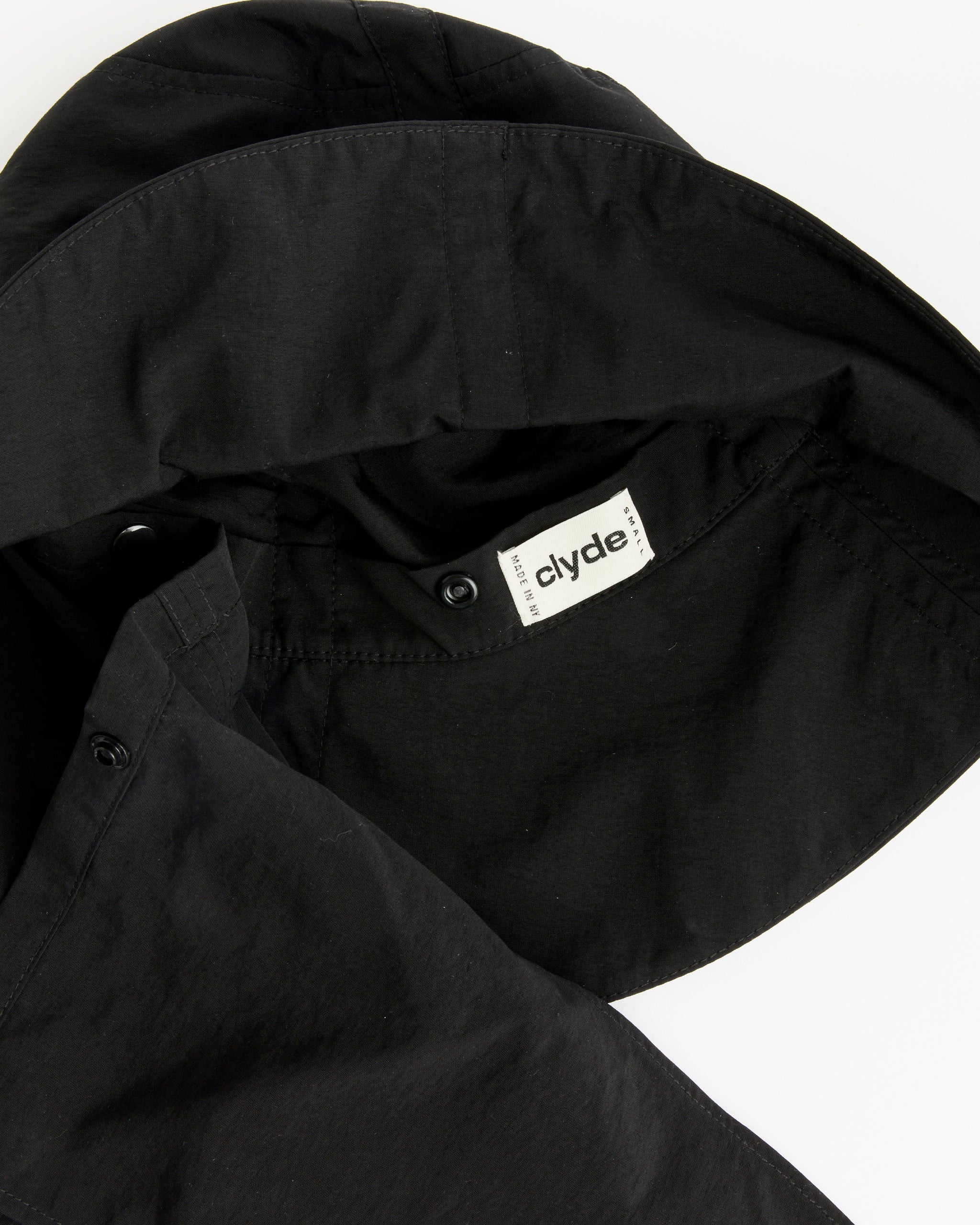 A close-up of a black hooded garment with an interior white Clyde tag, reminiscent of Clyde's Swim Bucket Hat in Black—a water-resistant nylon hat made in New York. The garment’s stitching and fabric texture are clearly visible.