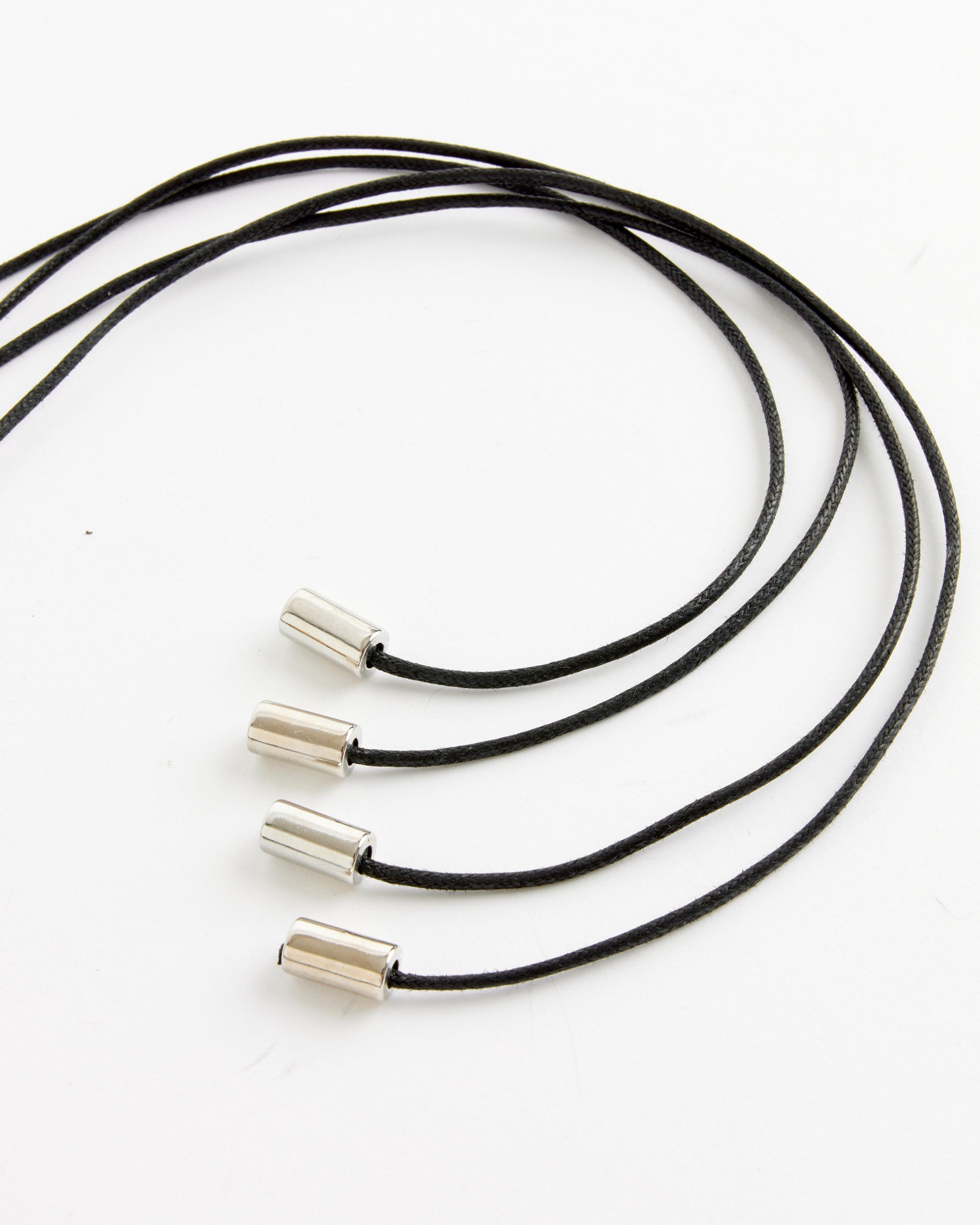 Four NOMIA Confetti Belts in Multi, each with black braided cords and silver cylindrical metal tips, are arranged in parallel curves on a white background.
