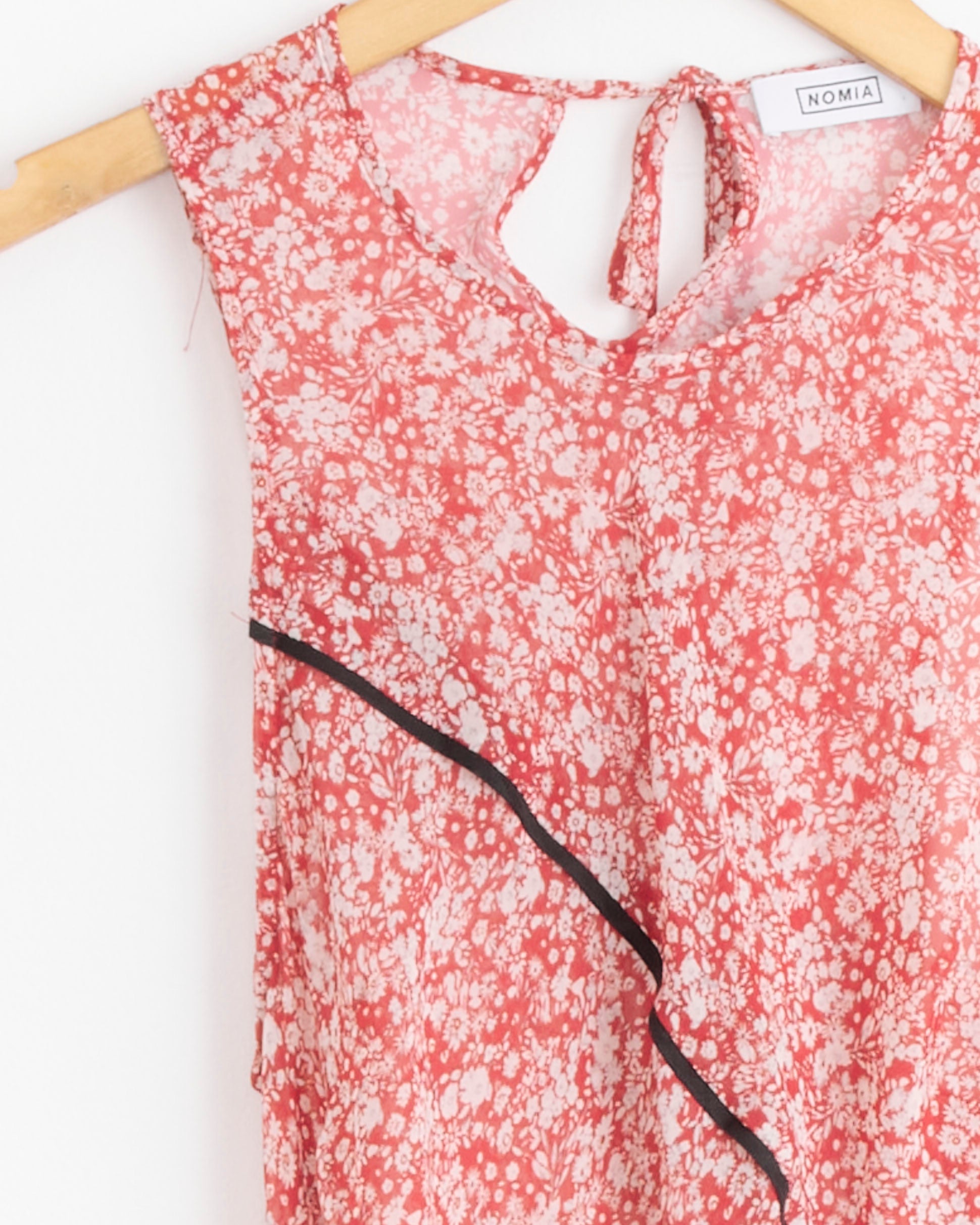 The NOMIA Paneled Bias Maxi Dress in Poppy Floral features a sleeveless design, keyhole tie neckline, and diagonal black trim, shown on a hanger.