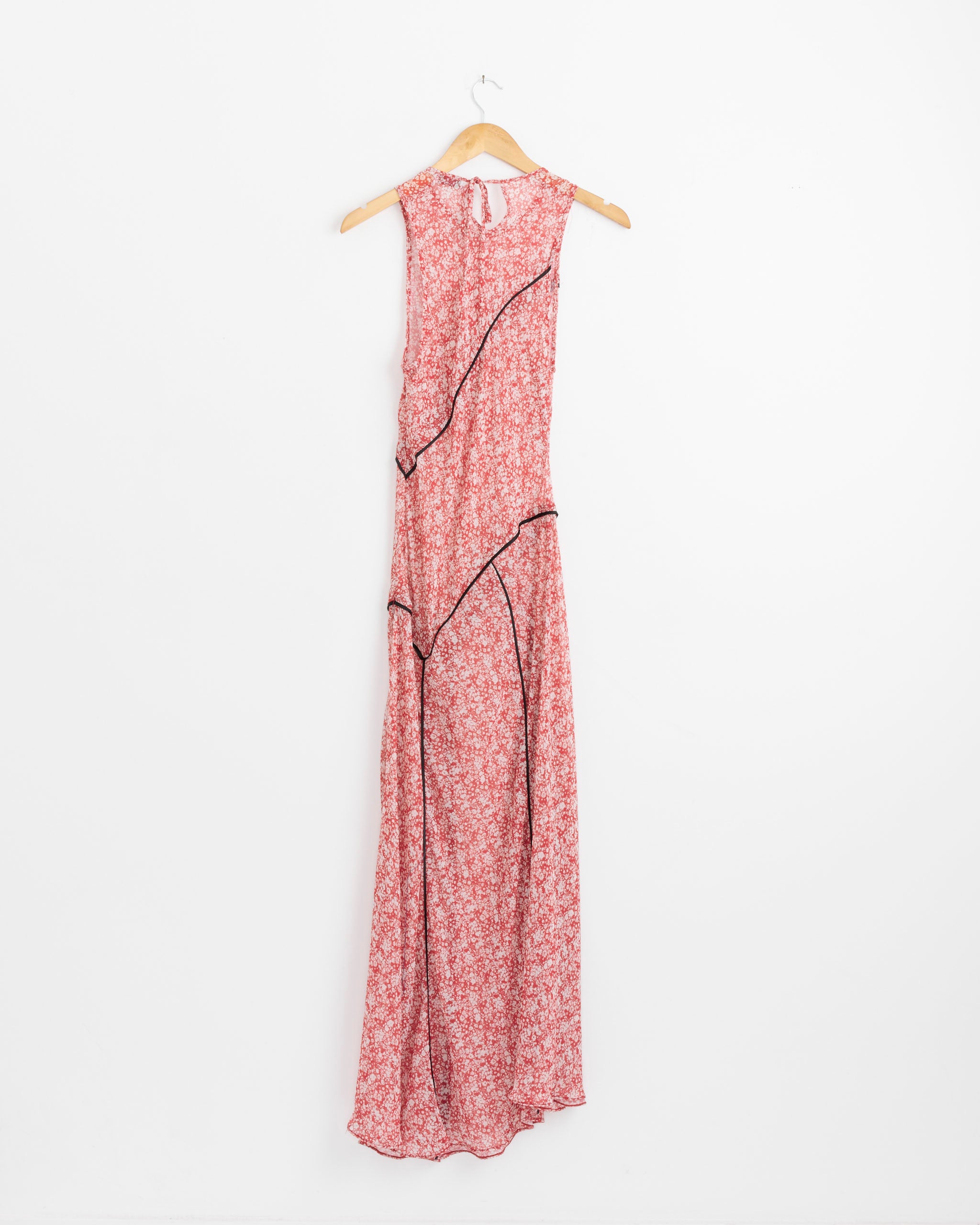 The NOMIA Paneled Bias Maxi Dress in Poppy Floral features a sleeveless, floor-length red design with a small white floral pattern, black trim accents, and a keyhole back, shown on a wooden hanger against a plain white background.