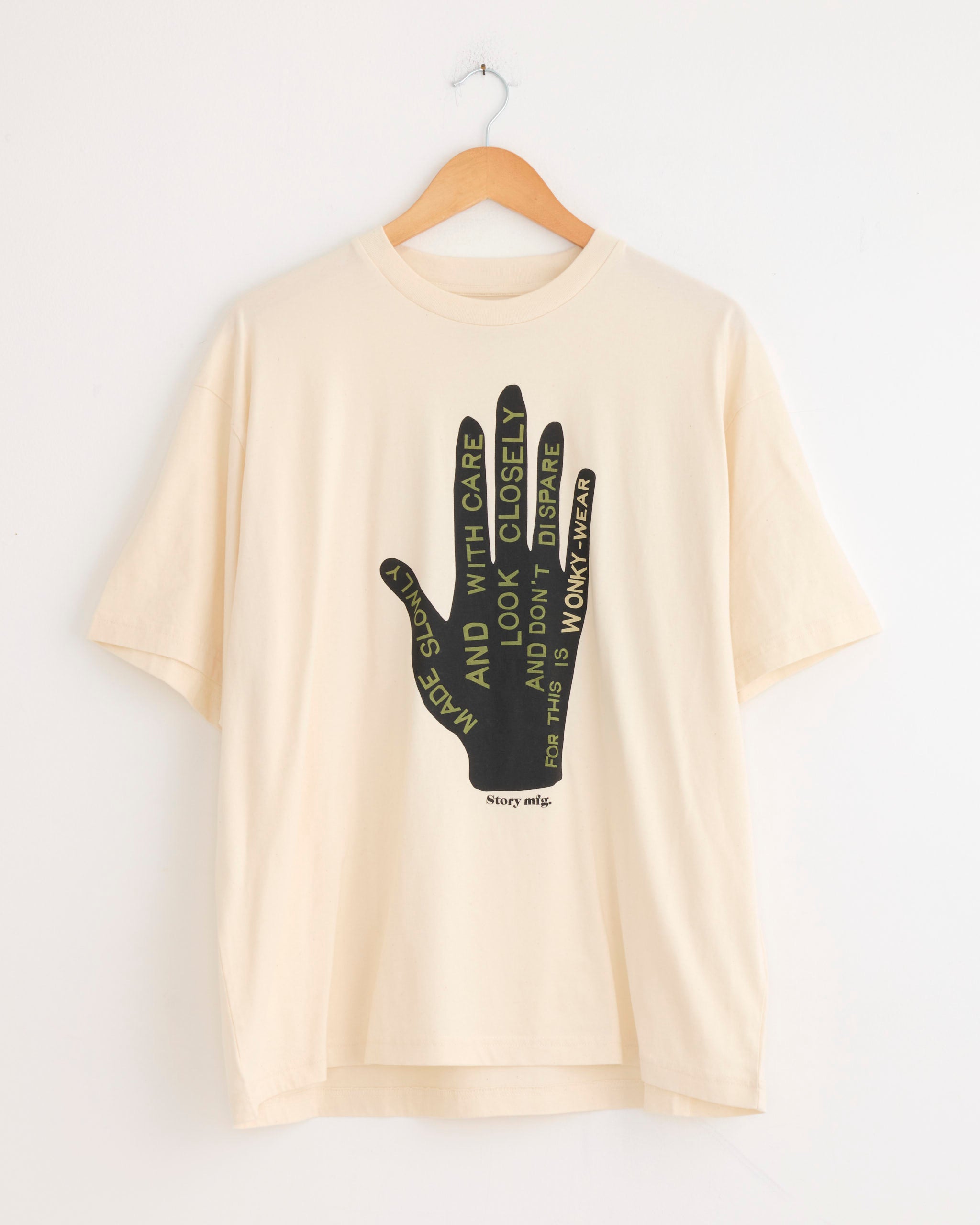 The Story mfg Grateful Tee in Made Slowly is an organic cotton, cream-colored shirt with a vintage fit, featuring a large black hand graphic and thoughtful text on the chest, plus the brand’s name below.