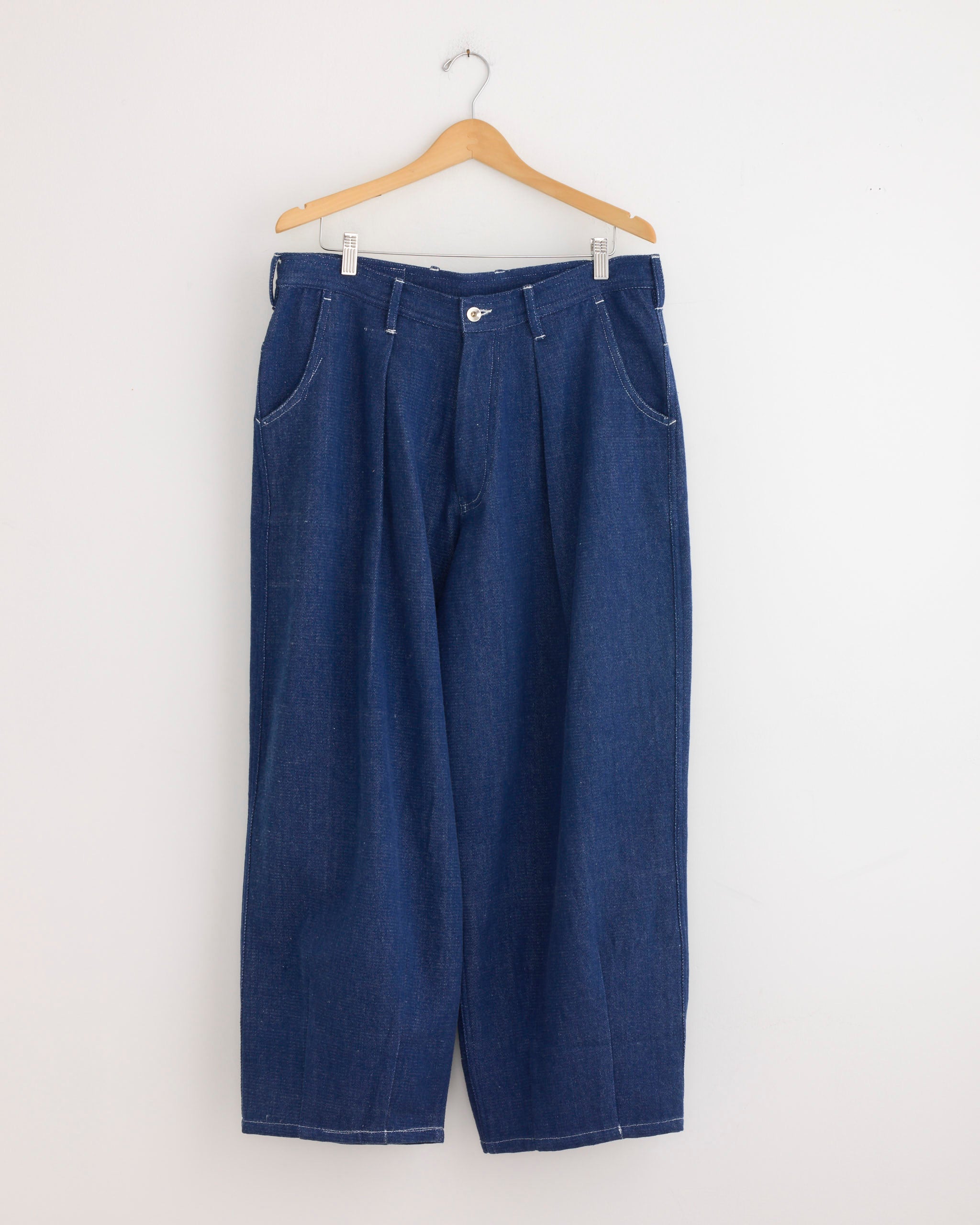 The Lush Jean in Handloom Denim by Story mfg, featuring a wide-leg cut and made from blue organic cotton, hangs on a wooden hanger against a plain white wall.