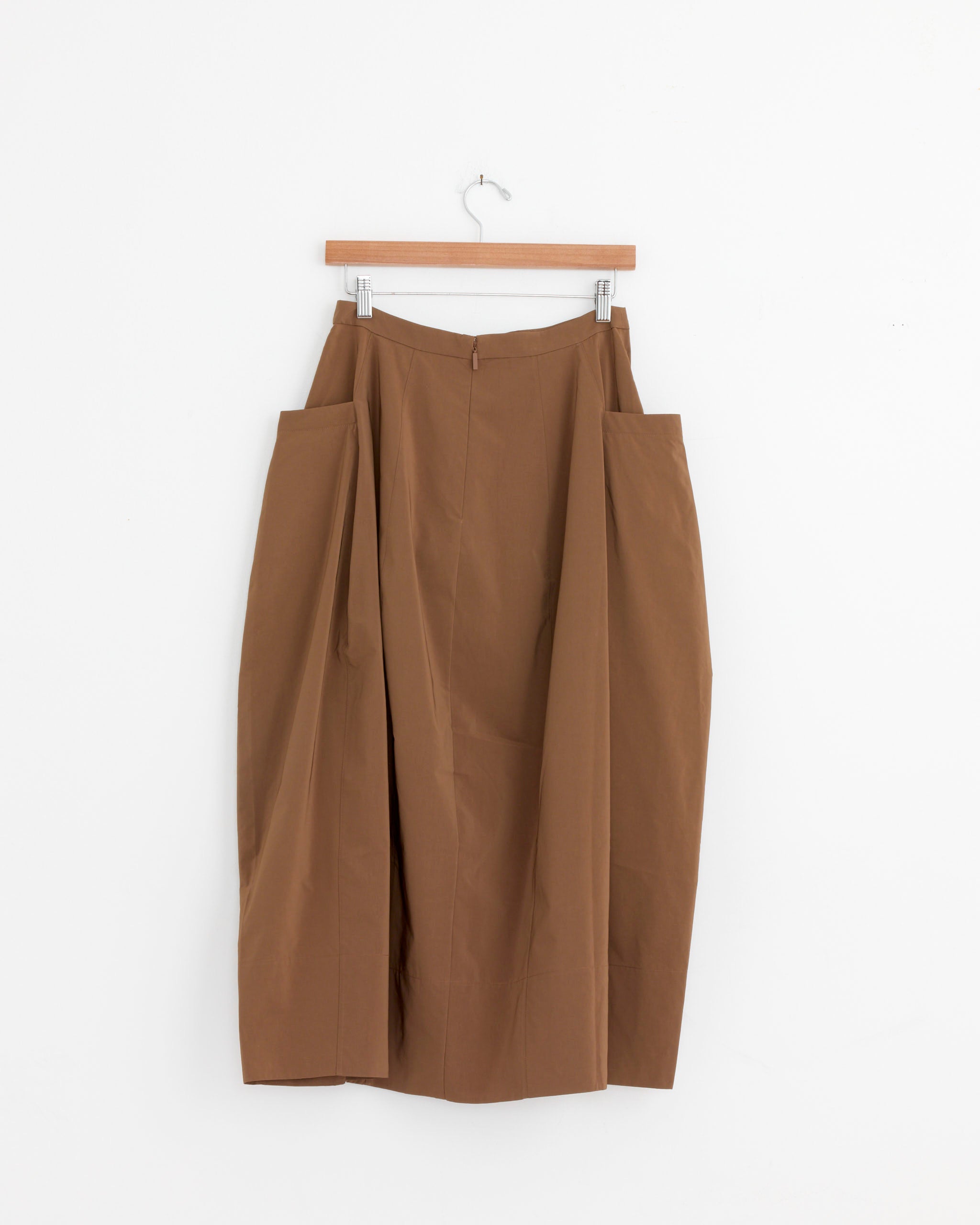 The Tibi Nylon Lantern Skirt in Caramel Latte, featuring a high waist and wide angular side panels for a sculptural silhouette, hangs on a wooden hanger against a plain white background.