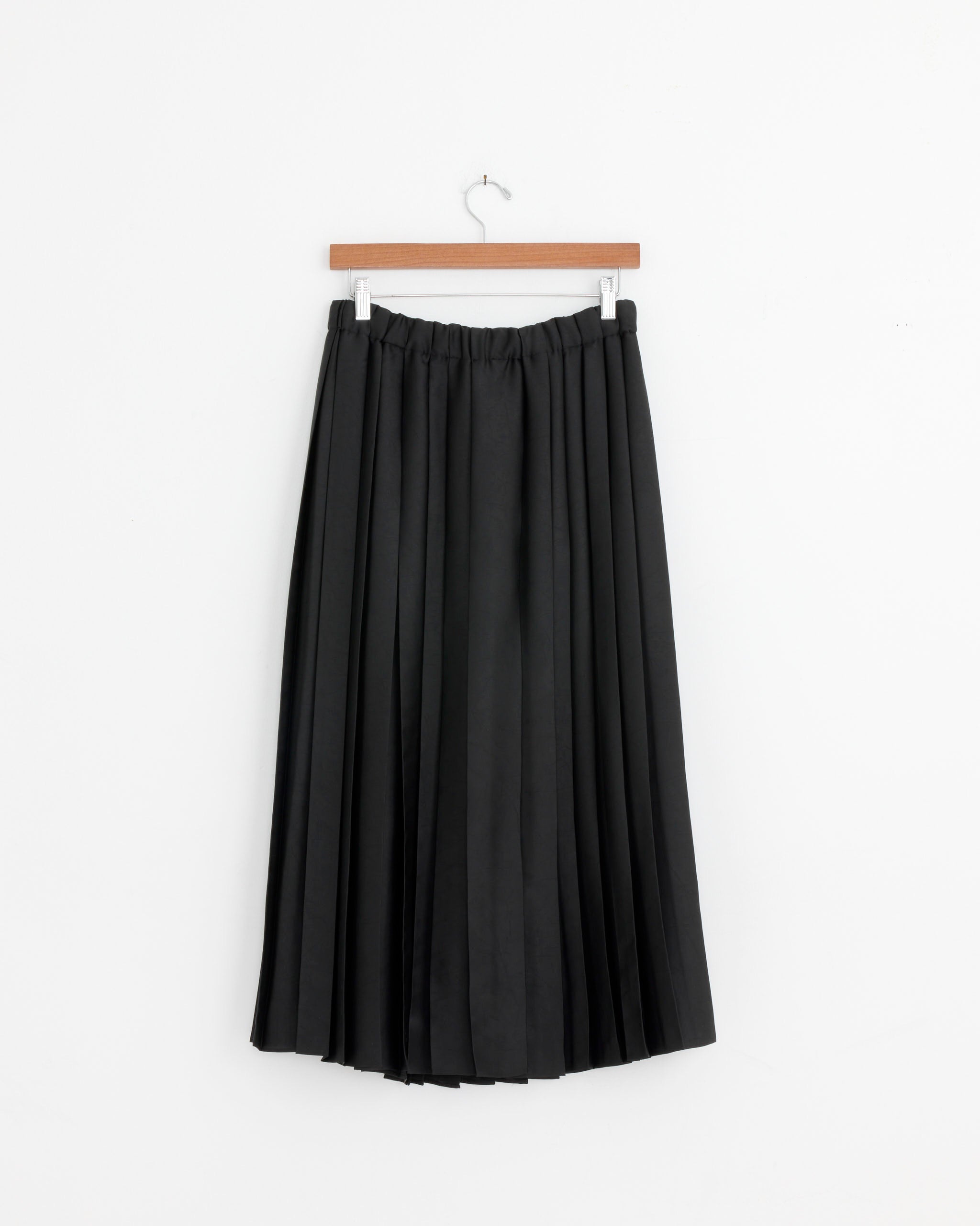 The Tibi Feather Weight Pleated Pull On Skirt in Black hangs on a wooden hanger against a plain white background.