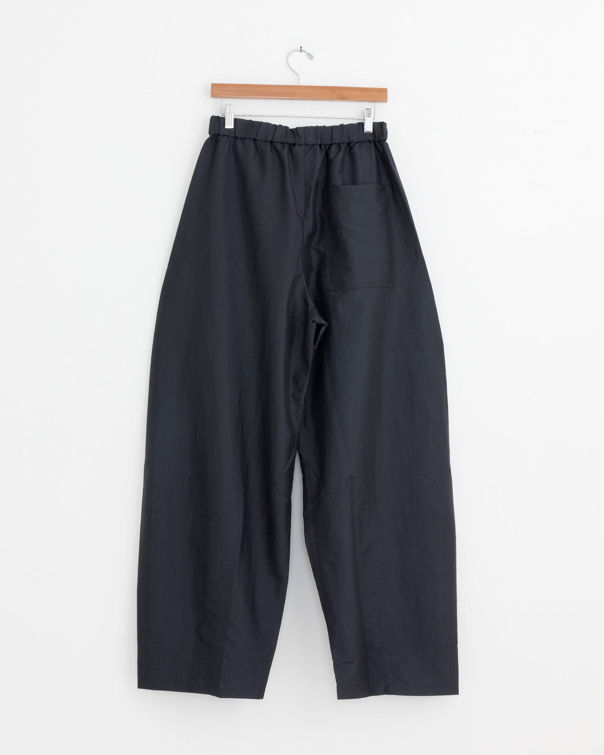 The Tibi Crispy Nylon Winslow Pant in Navy features a wide-leg silhouette, elastic waistband, and single back pocket, displayed on a wooden hanger against a plain white background.
