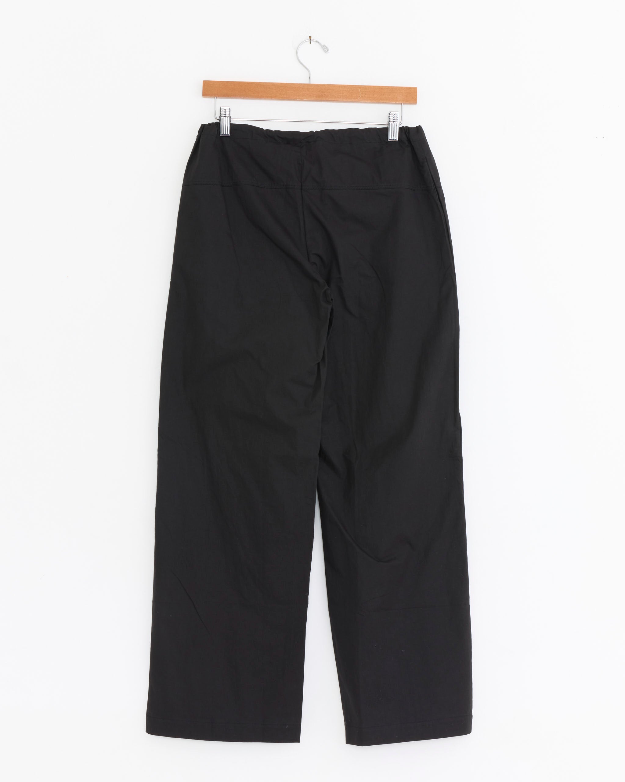 The Seam Pant in Black by Deiji Studios, crafted from organic cotton, hangs on a wooden hanger against a white background.
