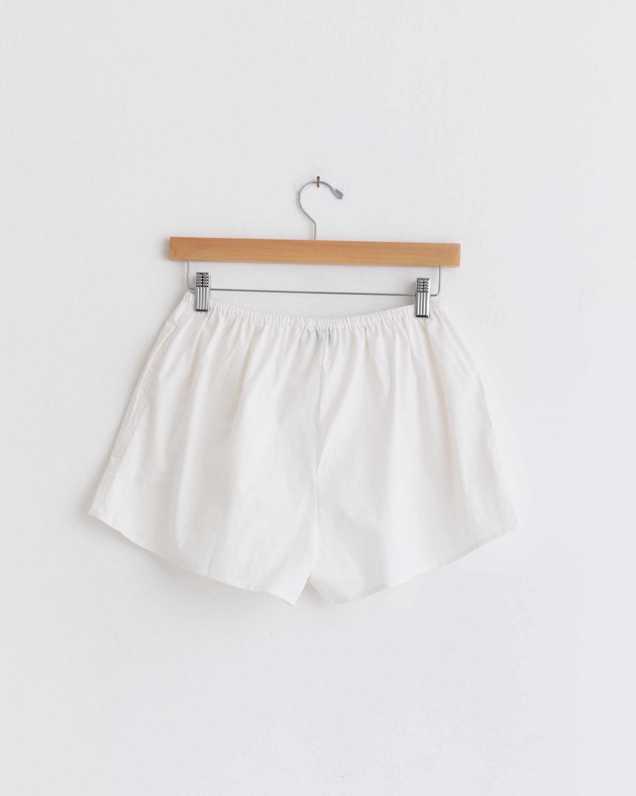 The Deiji Studios Round Collar Set in White Texture, crafted from organic cotton and featuring an elastic waistband, hangs on a wooden hanger against a plain white wall.