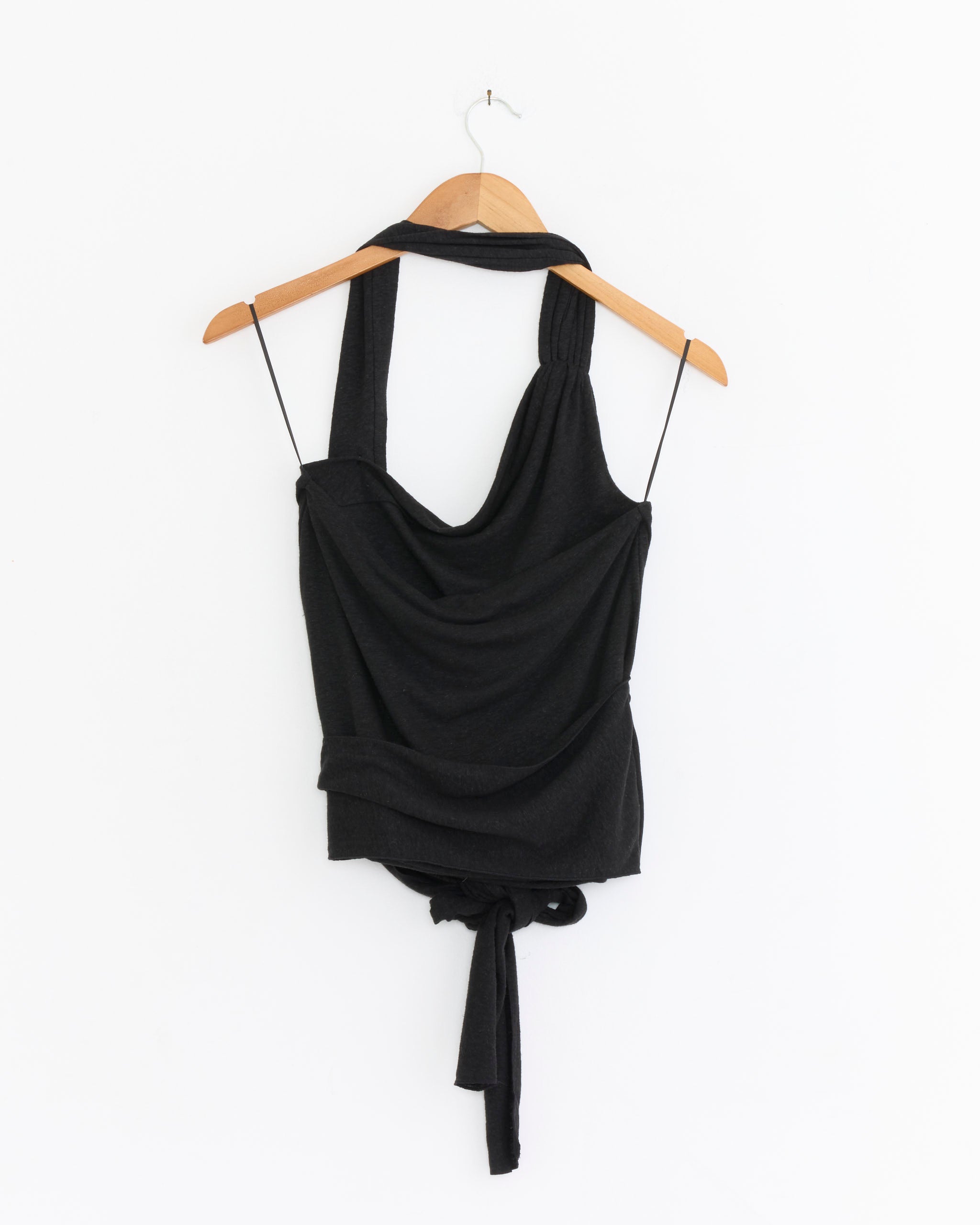 The Drape Halter Top in Black by Deiji Studios, with a draped neckline and waist tie, is shown on a wooden hanger against a white background.