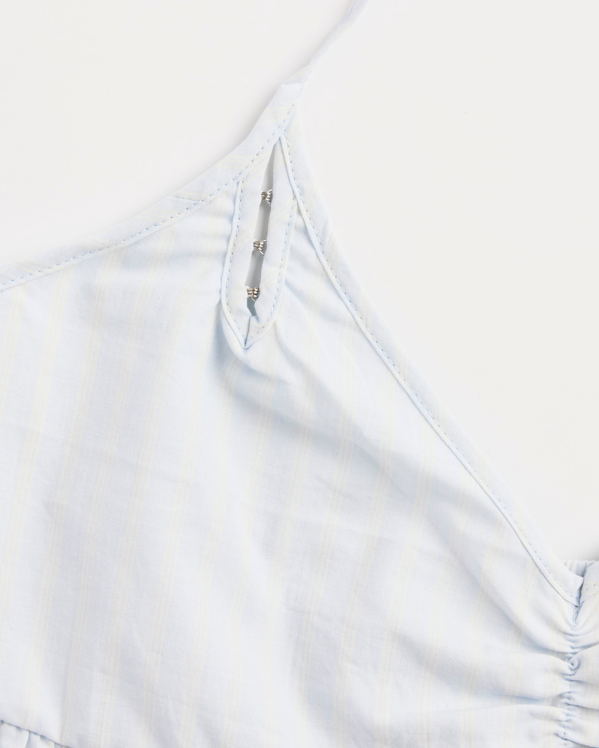Close-up of the Deiji Studios Keyhole Halter Top in Powder Blue Stripe—an organic cotton top with thin straps, silver hook-and-eye neckline closures, and a subtle striped pattern shown on a white background.