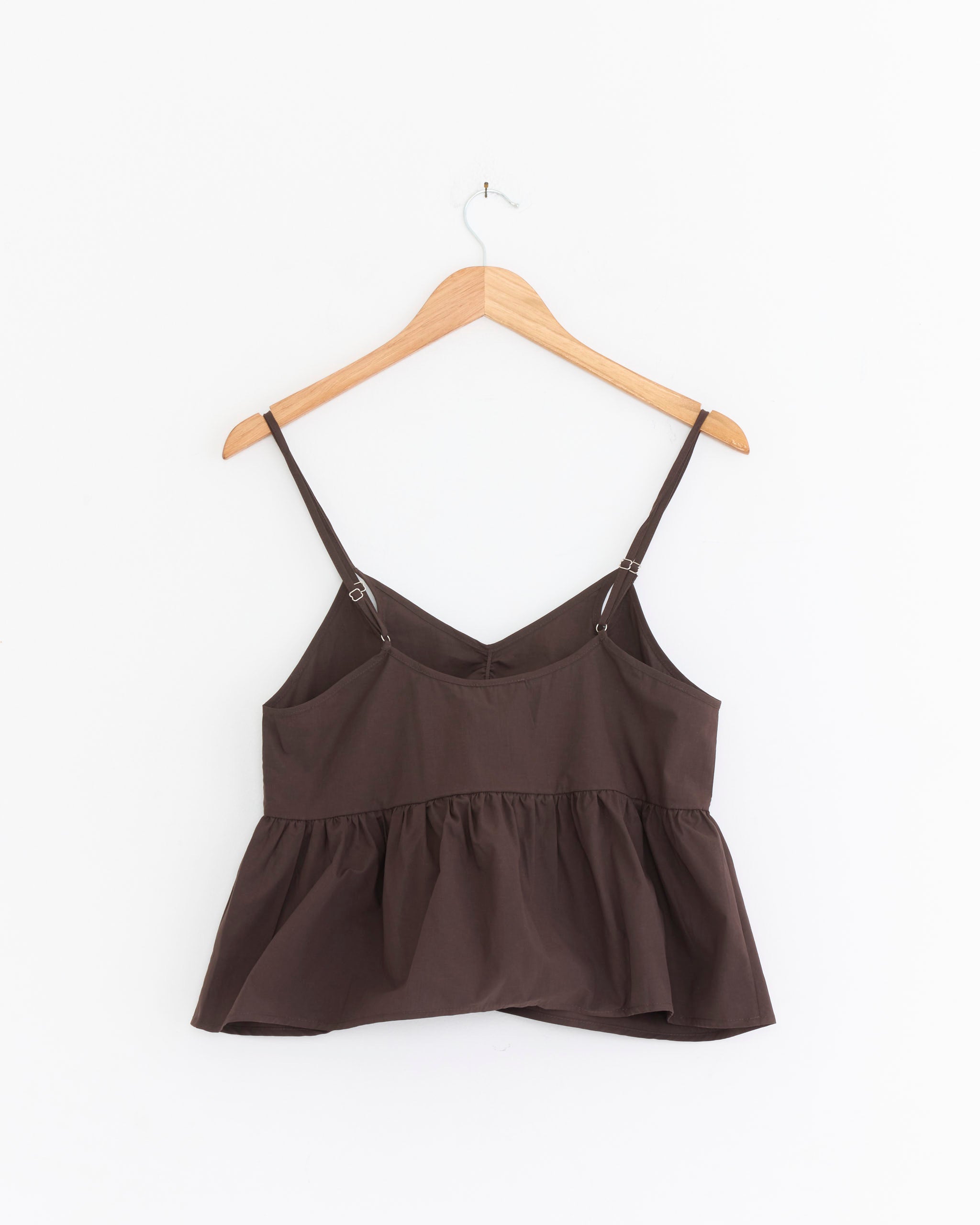 The Bind Set in Sepia by Deiji Studios features a brown sleeveless peplum cami with thin adjustable straps, shown on a wooden hanger against a white background—ideal paired as a chic top and bottom set.